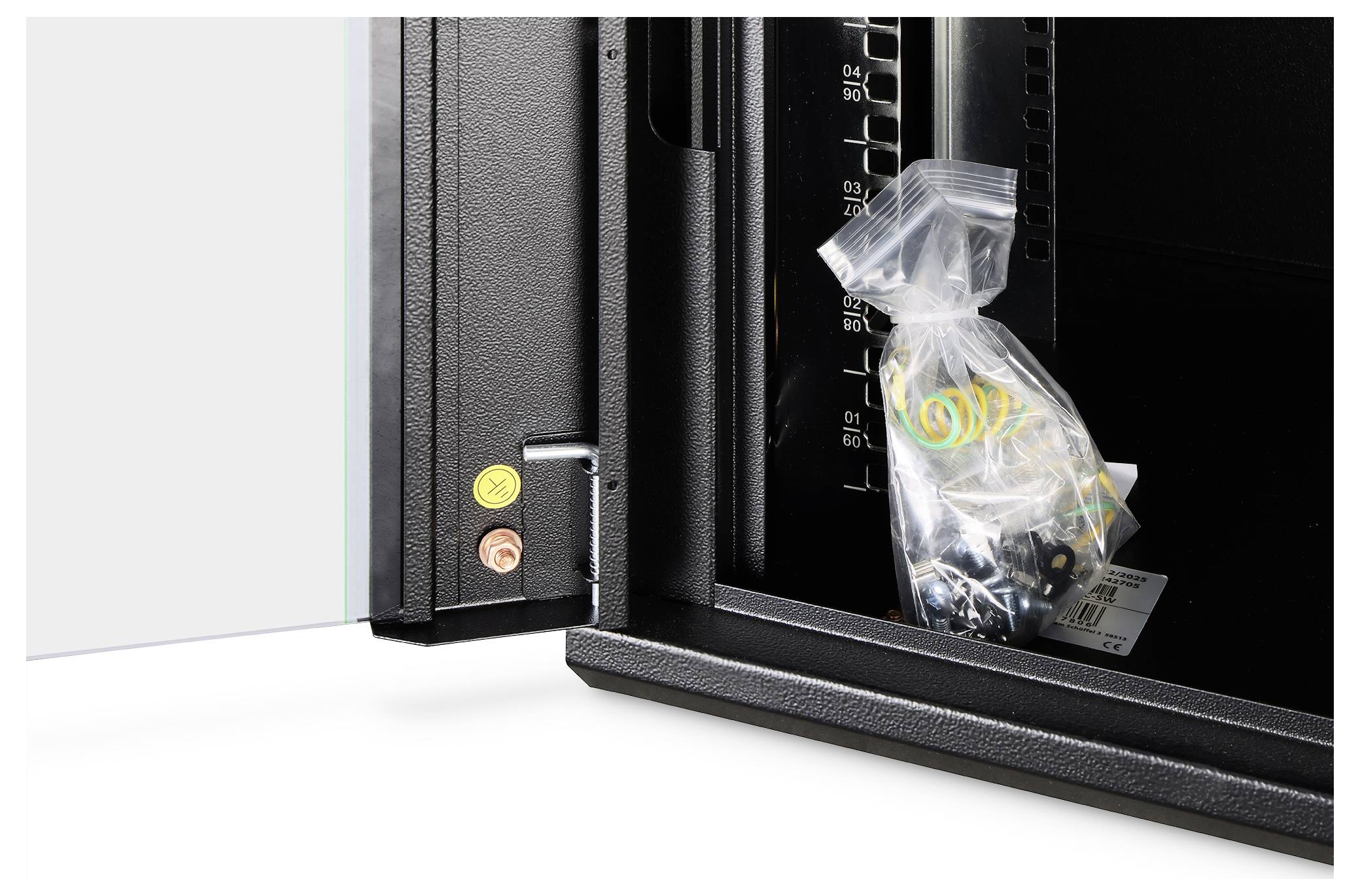 Eine offene Tresortür gibt den Blick frei auf eine Plastiktüte mit Schrauben und Dübeln im Inneren eines schwarzen Metallgehäuses mit Messskalen.