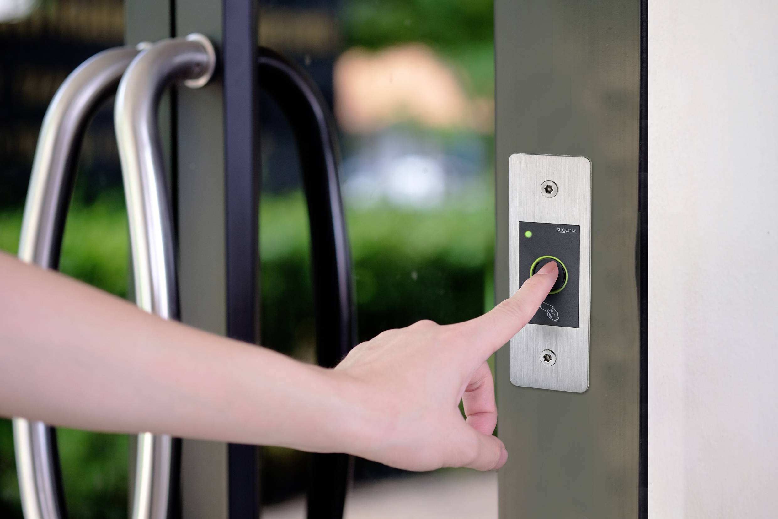 Eine Hand drückt einen Knopf auf einem Zugangskontrollfeld neben einer Glastür, um die Tür zu öffnen.