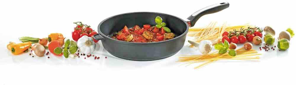 Eine Pfanne mit Tomatensauce und Kräutern ist von frischen Zutaten wie Paprika, Knoblauch, Tomaten und rohen Spaghetti umgeben.