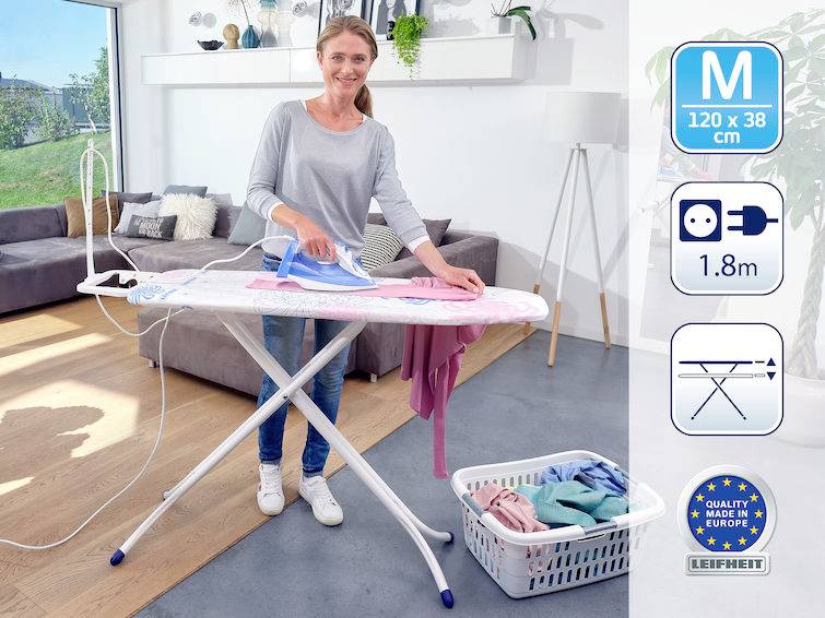 Eine Frau bügelt Wäsche auf einem Bügelbrett in einem modernen, hellen Wohnzimmer. Neben ihr ist ein Wäschekorb mit Kleidung.