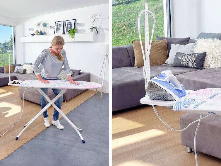 Frau bügelt Kleidung auf einem Bügelbrett in einem Wohnzimmer mit Sofa und Kissen. Helle, moderne Einrichtung mit großer Fensterfront.