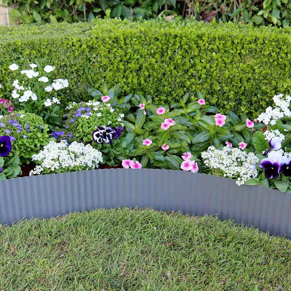 Ein blühendes Gartenbeet mit farbigen Blumen, umgeben von einem gepflegten Rasen und einer Hecke im Hintergrund.