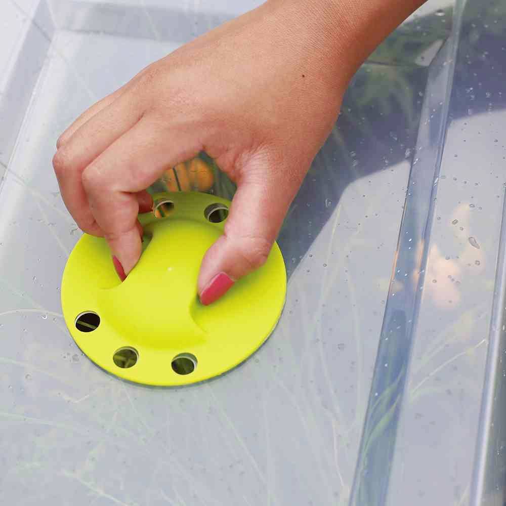 Eine Hand platziert einen gelben, runden Deckel mit Lüftungslöchern auf einem durchsichtigen Behälter.