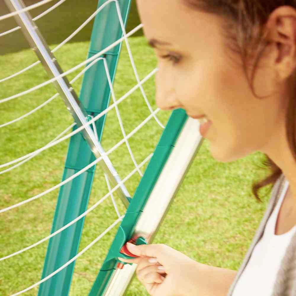Eine Person dreht einen grünen Knopf an einem netzartigen Gartengerät im Freien. Das Gerät scheint zum Sammeln von Blättern oder Kletterpflanzen geeignet zu sein.