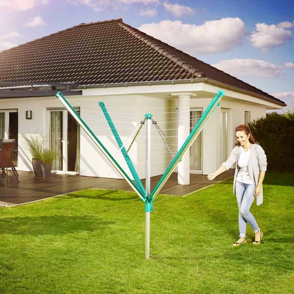Eine Frau in einem Garten spannt einen blauen Wäscheschirm neben einem Haus auf.