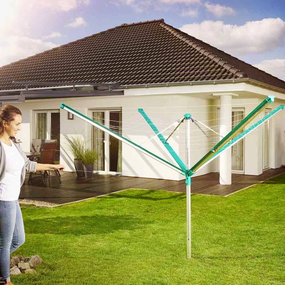 Eine Frau steht in einem Garten vor einem modernen Haus und betrachtet einen grünen Wäscheschirm auf dem Rasen.