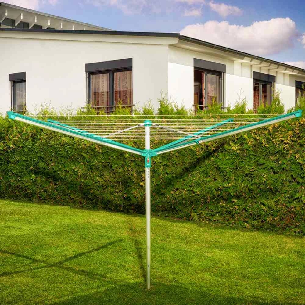 Grüner Wäscheständer im Garten vor einer Hecke und einem weißen Haus bei sonnigem Wetter.