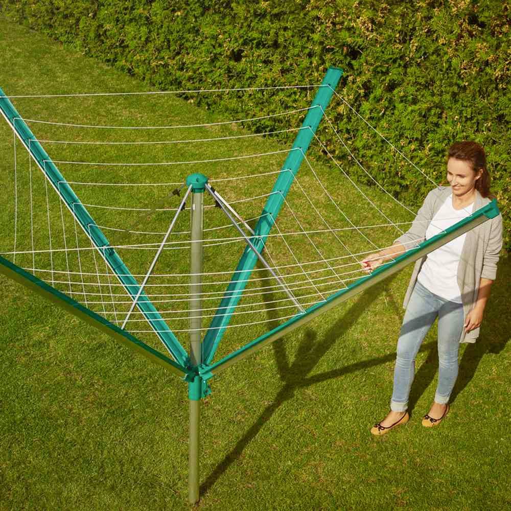 Frau steht neben einem grünen Wäscheschirm im Garten. Sie schaut auf die Leinen, vor einer grünen Hecke. Es ist sonnig draußen.