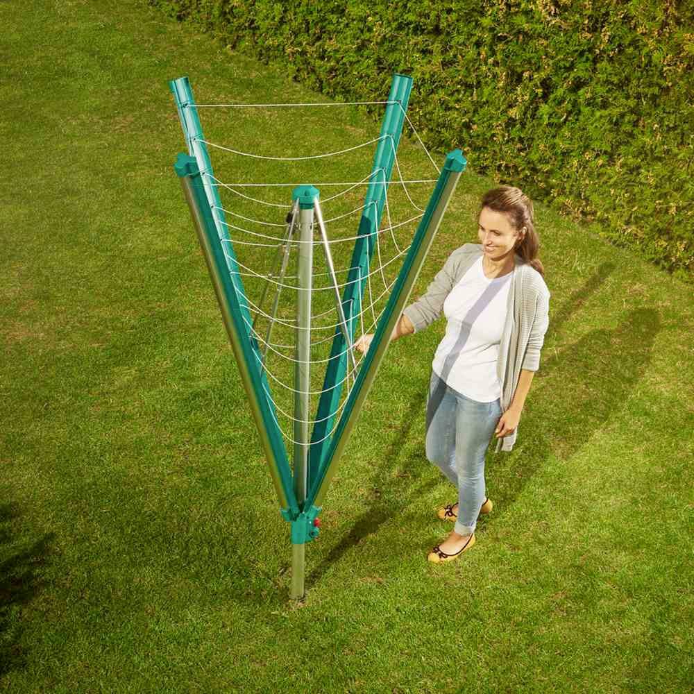 Eine Frau steht im Garten neben einem grünen, geöffneten Wäscheständer mit mehreren Leinen, bereit zum Aufhängen von Wäsche.