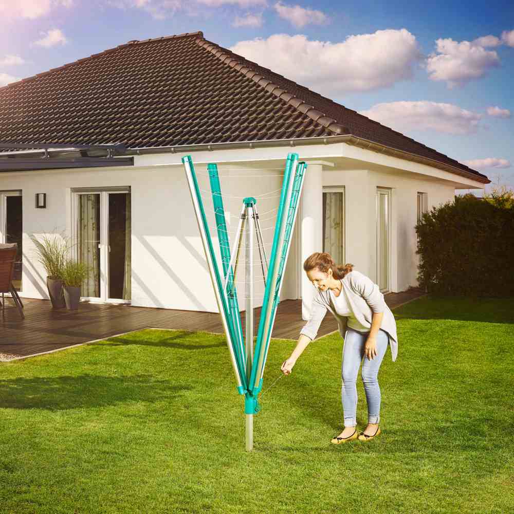 Eine Frau befestigt eine Wäschespinne im Garten vor einem modernen Einfamilienhaus unter blauem Himmel.