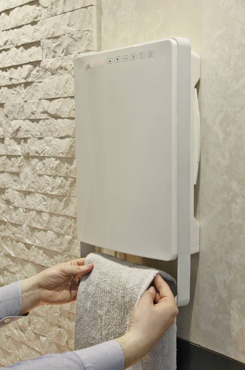 Eine Person trocknet ein Handtuch unter einem an der Wand montierten elektrischen Handtuchwärmer in einem Badezimmer.