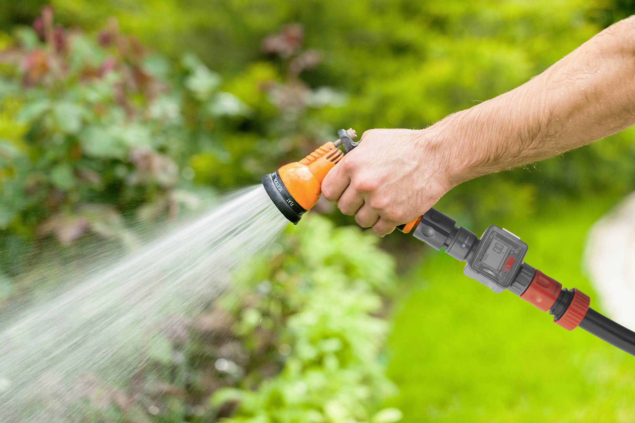 Eine Person hält einen Gartenschlauch und bewässert Pflanzen in einem grünen Garten.