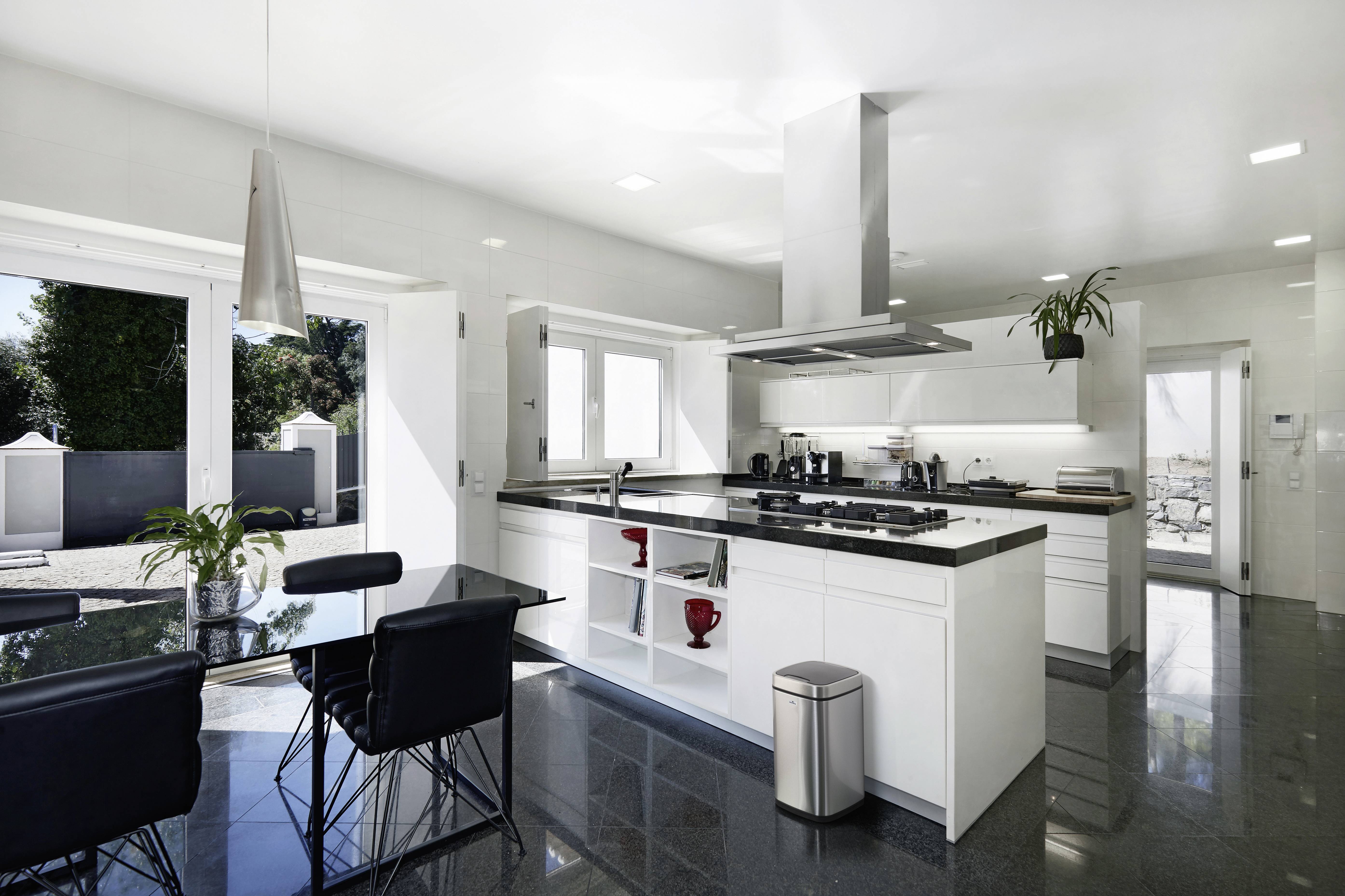 Moderne Küche mit weißer Einrichtung, großem Fenster und Esstisch. Helle, offene Gestaltung mit Pflanzen und Edelstahlakzenten.