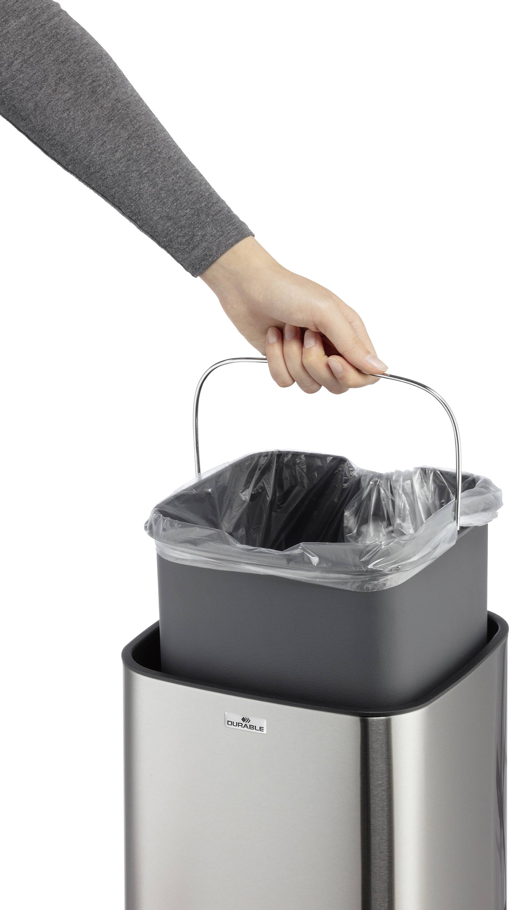 Eine Hand zieht einen mit Müllsack ausgestatteten Inneneimer aus einem silbernen Mülleimer.