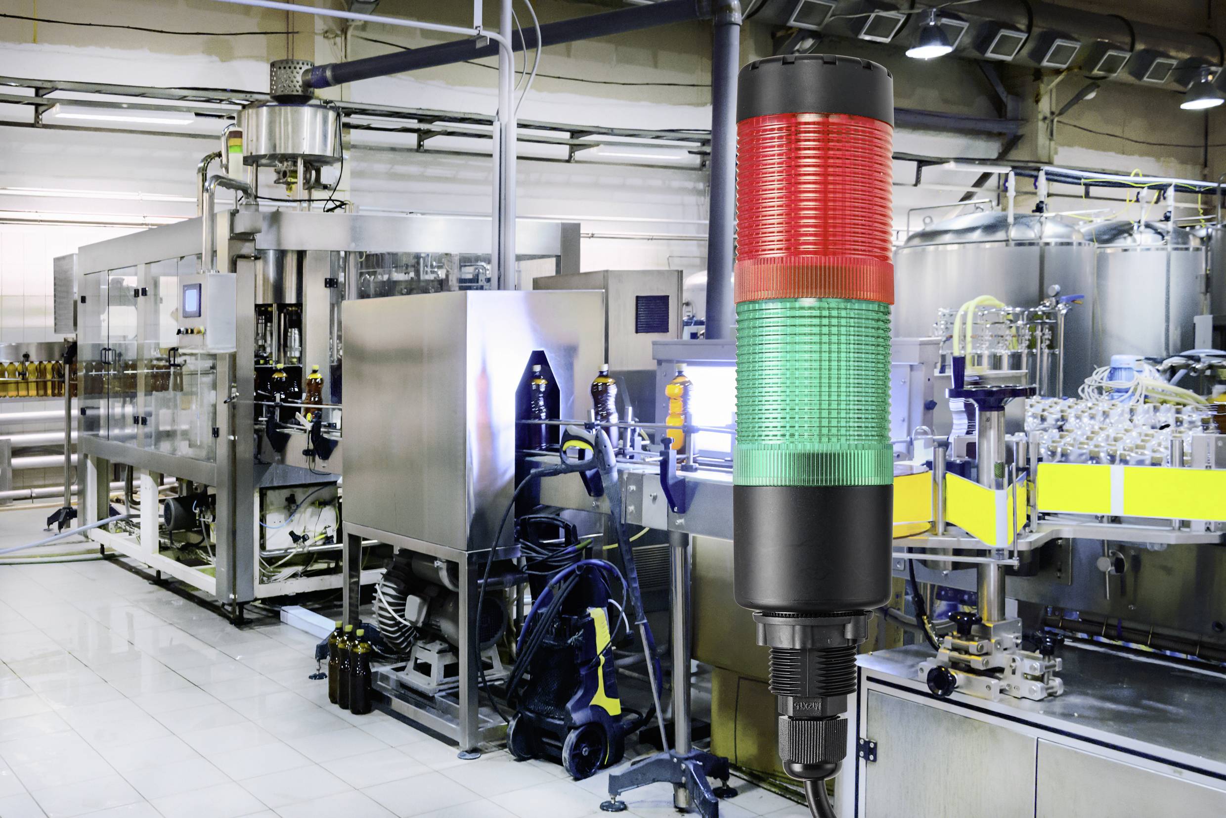 Automatisierte Produktionsanlage mit einem dreifarbigen Signalleuchten-Turm im Vordergrund, der Statussignale anzeigt.