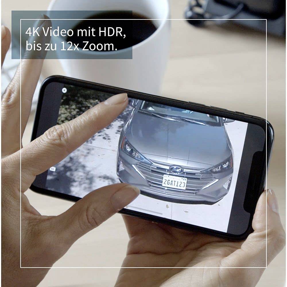 Eine Person zoomt in einem 4K-Video auf einem Smartphone auf ein Autokennzeichen. Text im Bild: '4K Video mit HDR, bis zu 12x Zoom.'