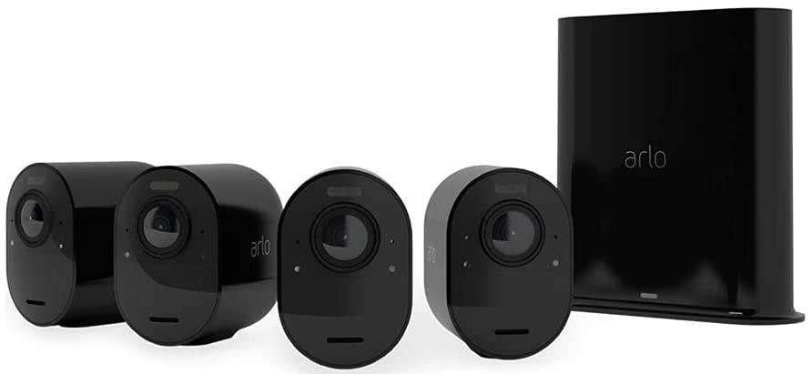 Vier schwarze Überwachungskameras der Marke Arlo vor einer schwarzen Basisstation, nebeneinander angeordnet.