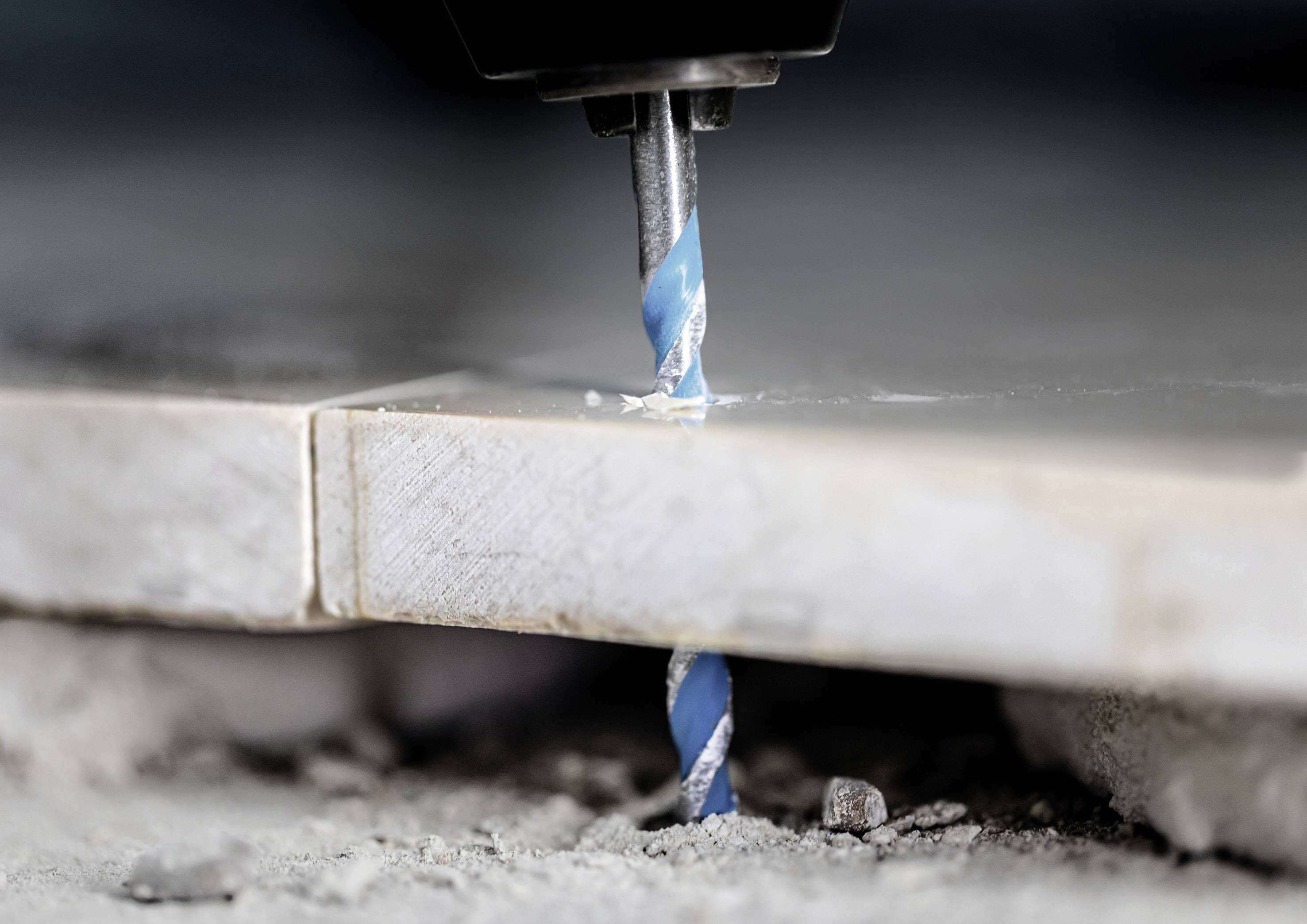 Bohren in Fliesen mit einem Bohrer auf einer Baustelle. Staub und Splitter um das Bohrloch herum.