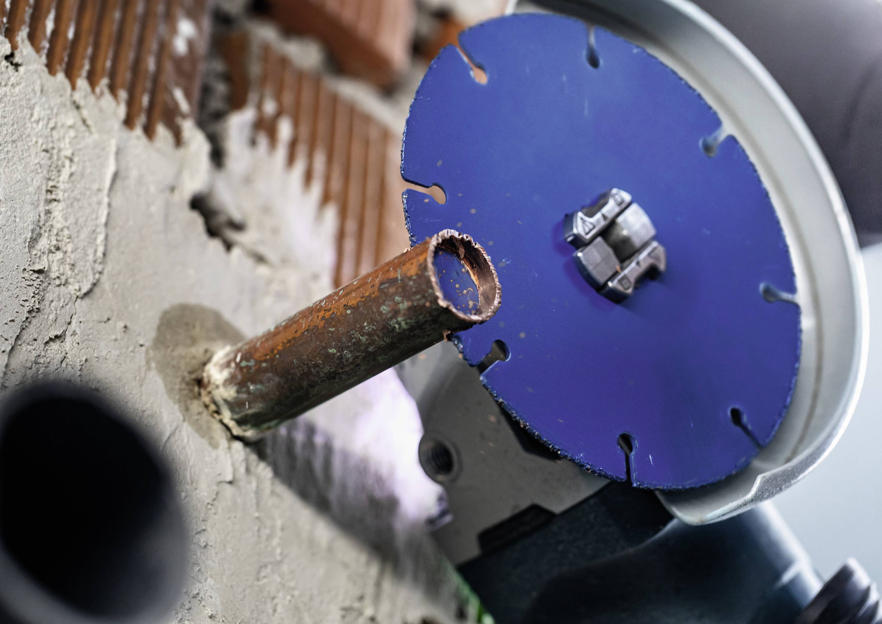 Eine Trennschleifer-Scheibe schneidet ein Metallrohr, das aus einer Betonwand herausragt. Staubpartikel in der Luft.