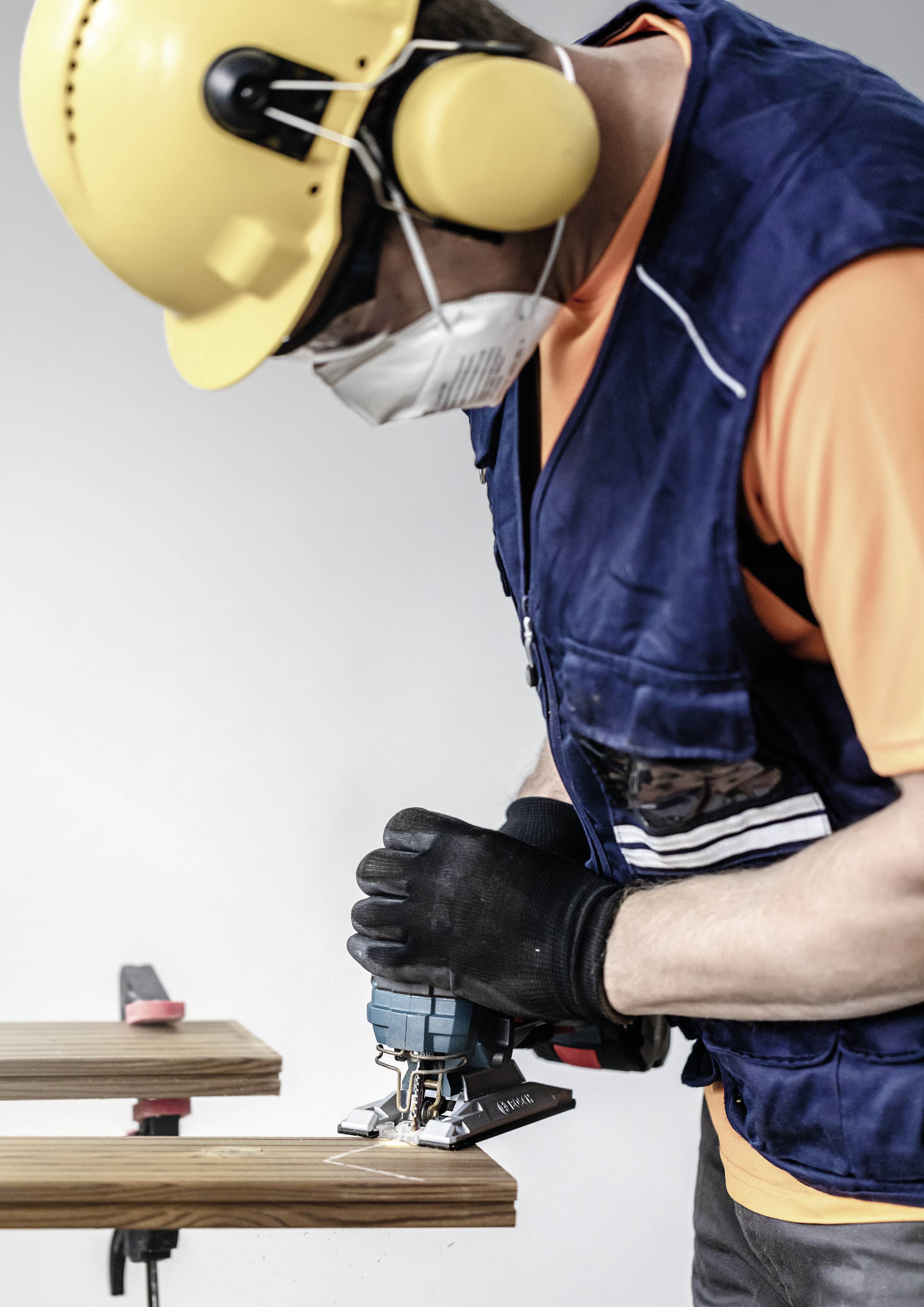 Ein Arbeiter mit Helm, Gehörschutz und Maske sägt Holz mit einer Elektrosäge.