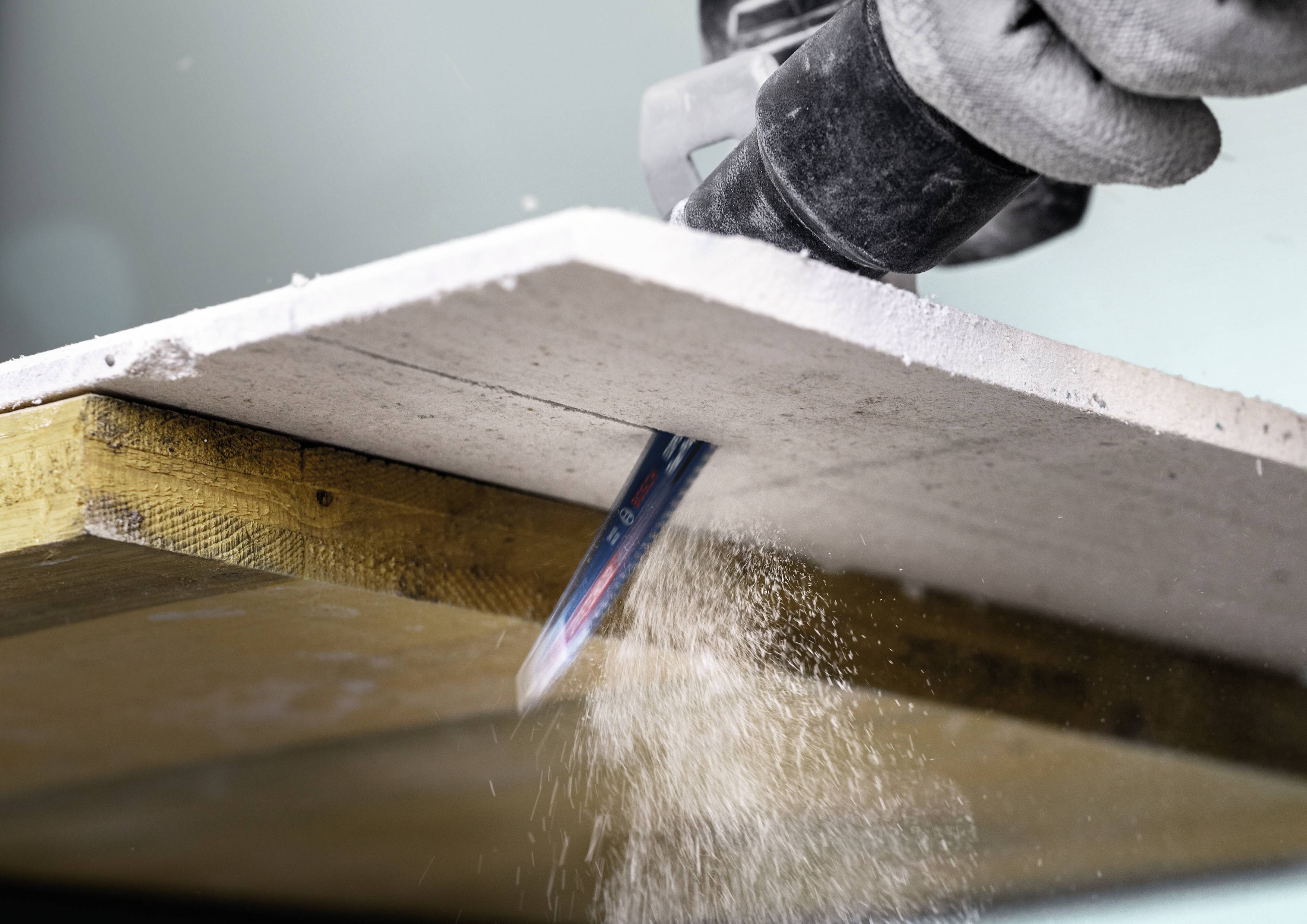 Person schneidet mit einer Maschine durch eine weiße Platte, Staub fliegt von der Schnittstelle.