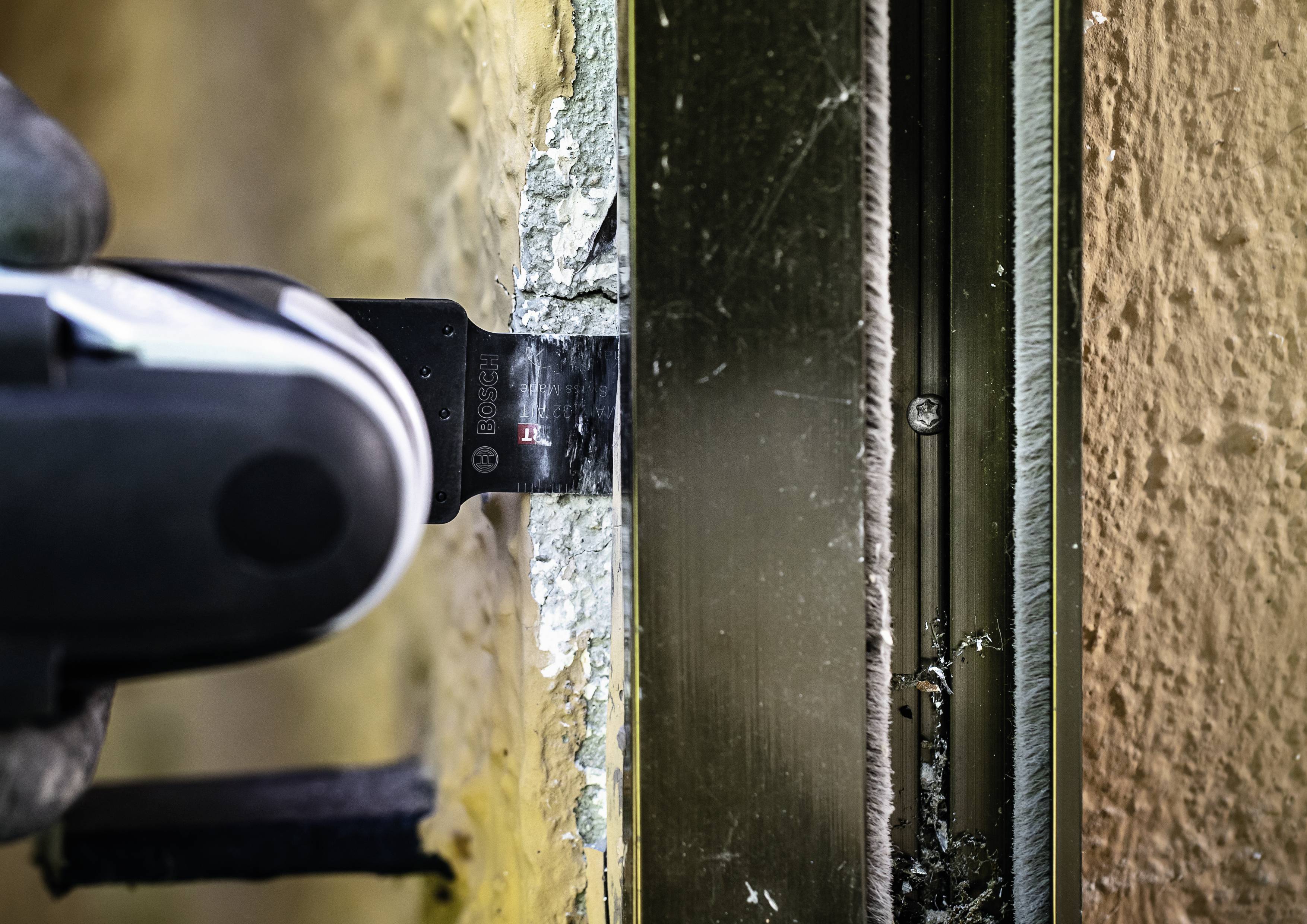 Ein Handwerker schneidet mit einer elektrischen Säge durch Metall an einer Kante, umgeben von Beton- oder Putzwand.