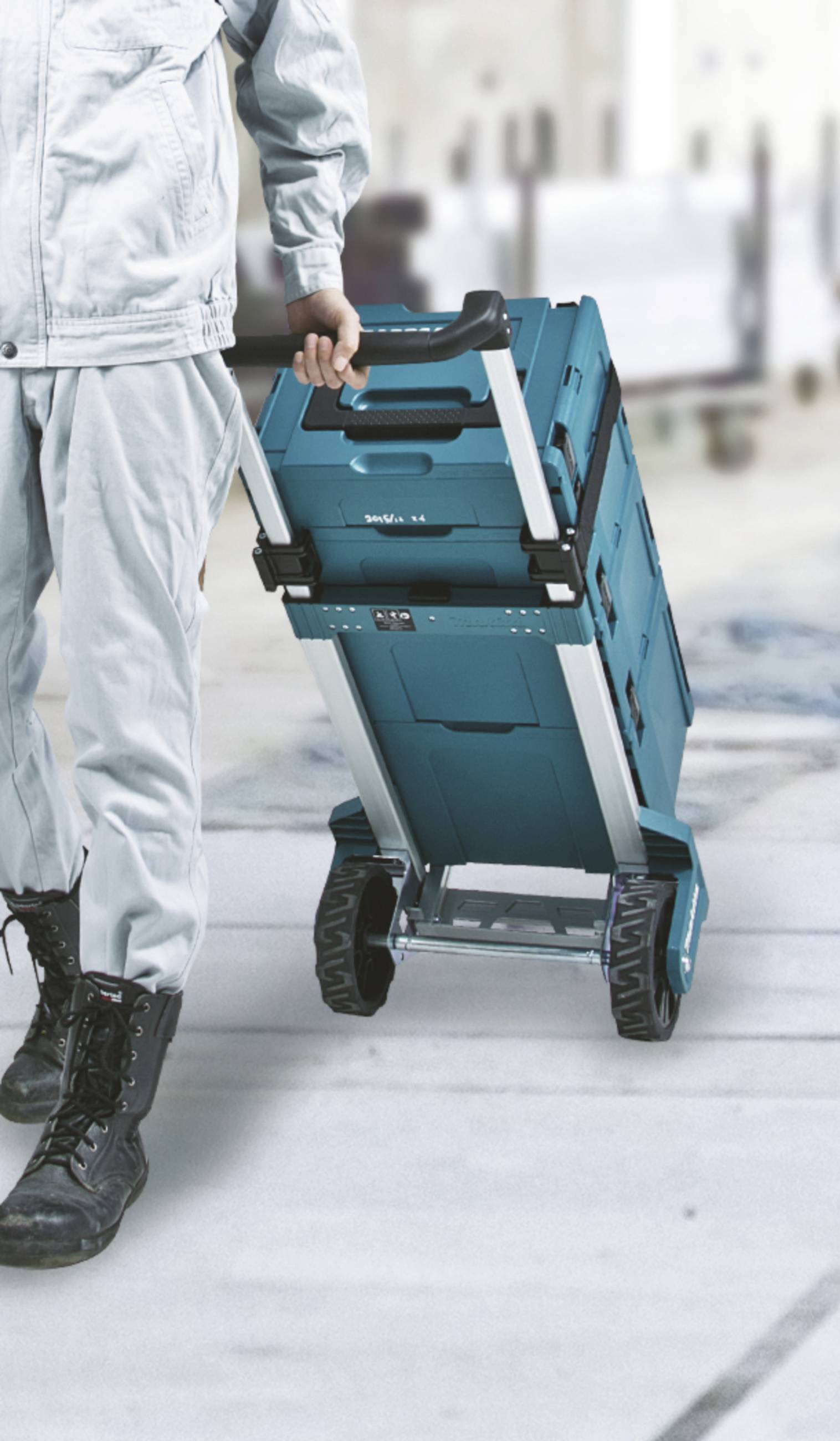 Eine Person in Arbeitskleidung zieht einen blauen Rollwagen auf einem Industrieboden.