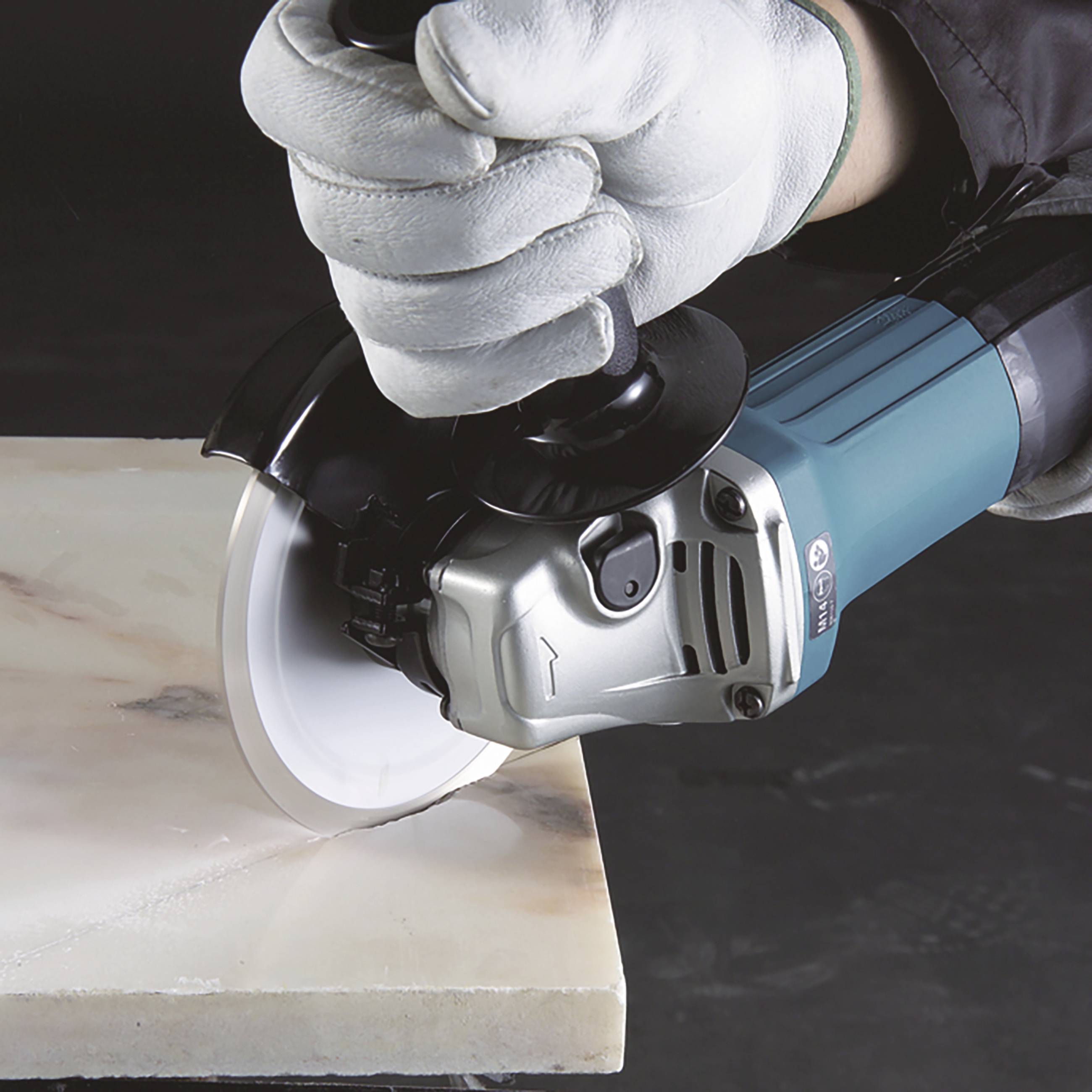 Ein Arbeiter in weißen Handschuhen schneidet mit einem Winkelschleifer eine Marmorplatte.