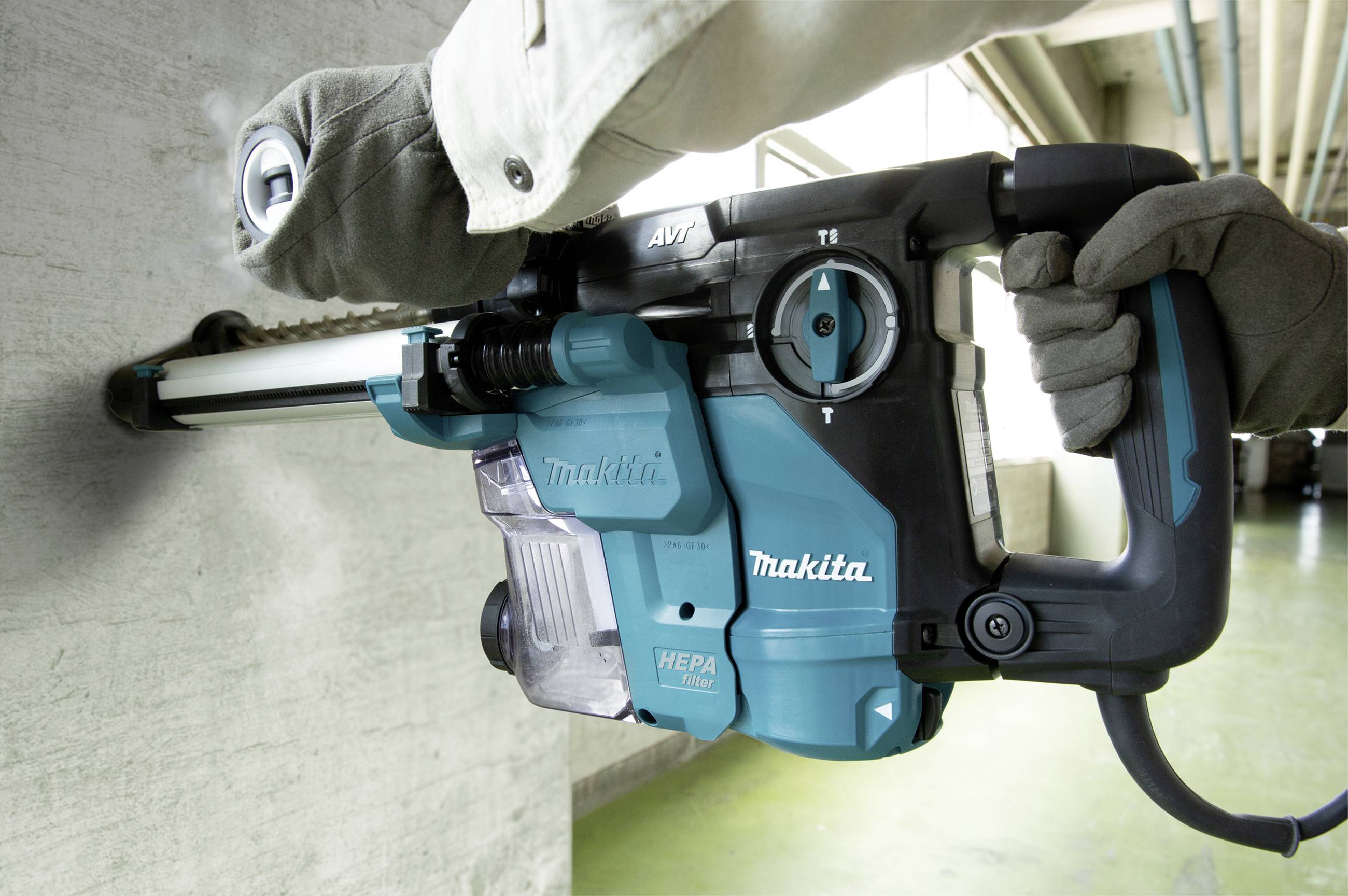 Eine Person bohrt mit einem blauen Bohrhammer mit HEPA-Filter in eine Betonwand.