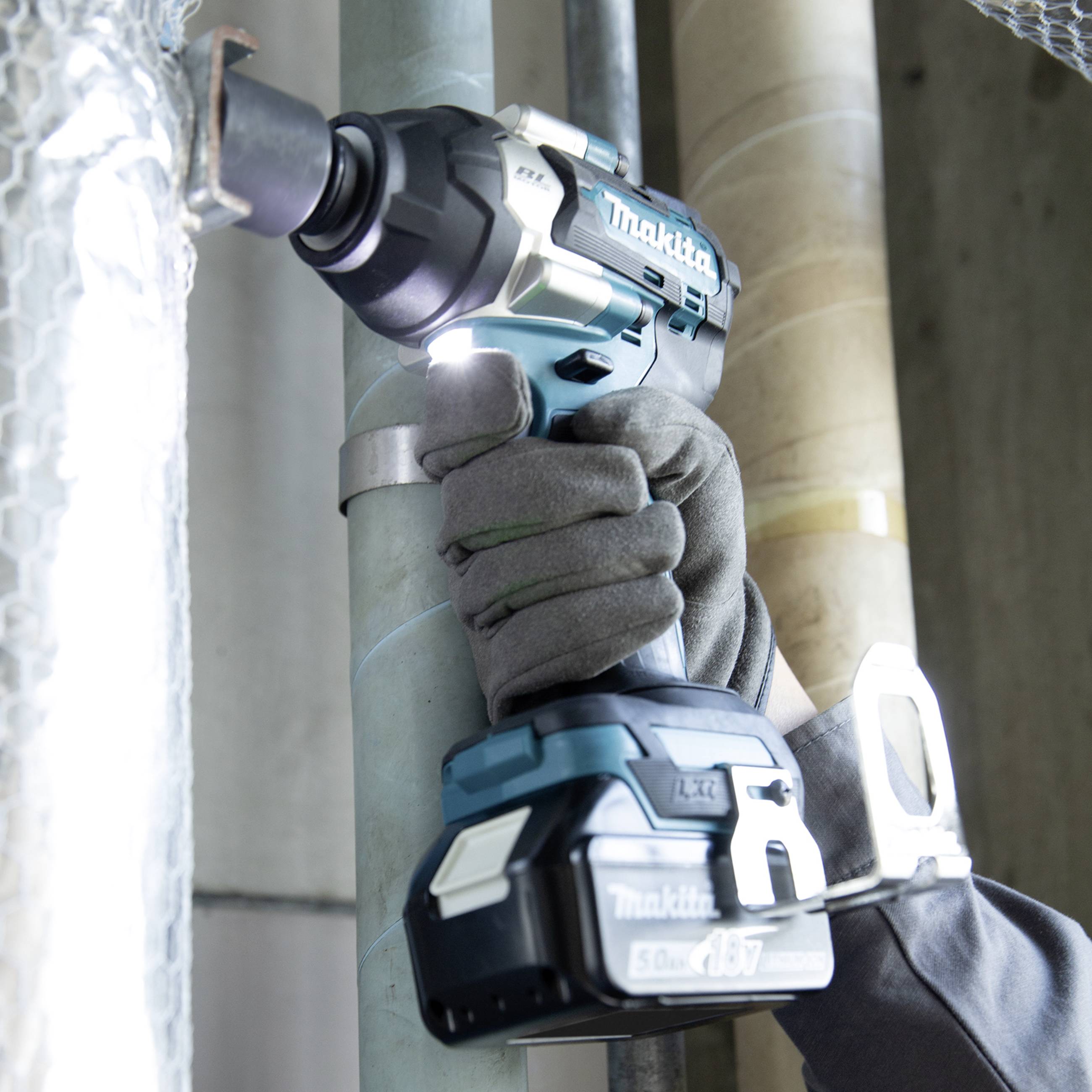 Eine Hand mit Handschuh bedient einen elektrischen Schraubenschlüssel, der an einem metallischen Rohr arbeitet.