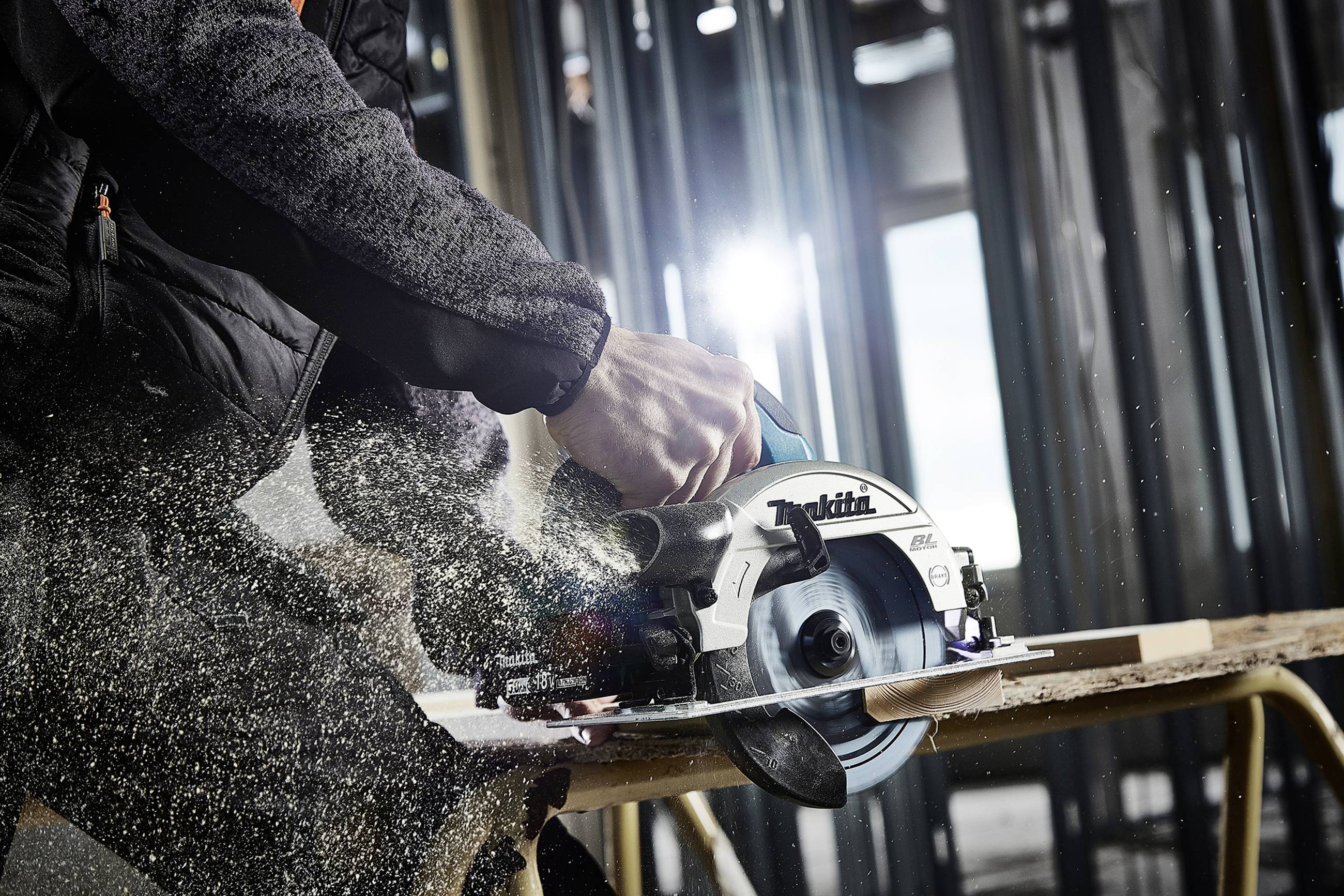 Eine Person schneidet mit einer elektrischen Kreissäge ein Holzstück. Sägespäne fliegen durch die Luft.