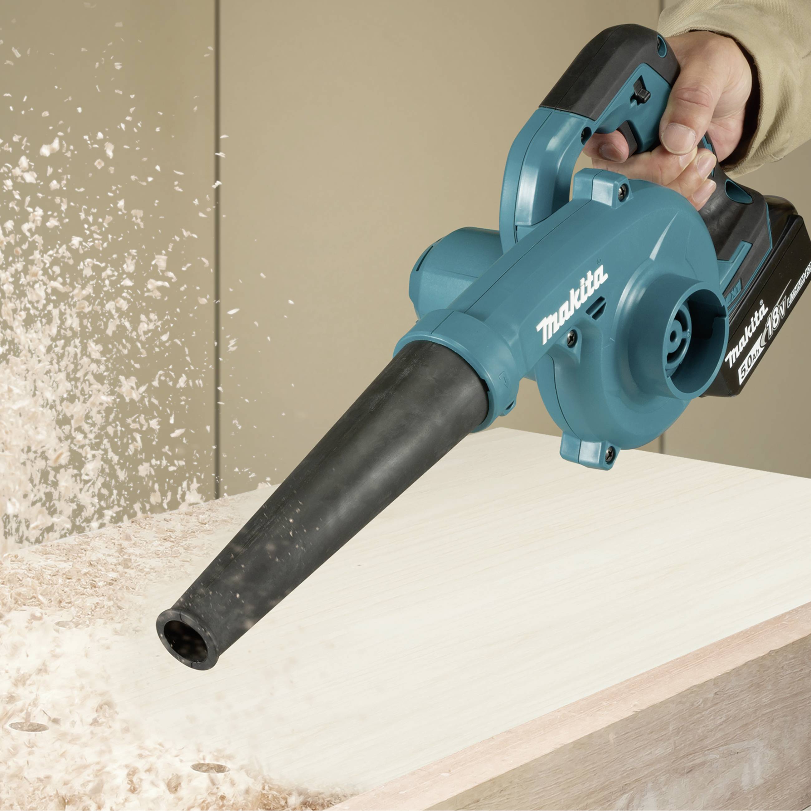 Eine Person hält ein blau-schwarzes, Marken-gelabeltes Elektrowerkzeug, um Holzspäne von einer Holzplatte zu entfernen.