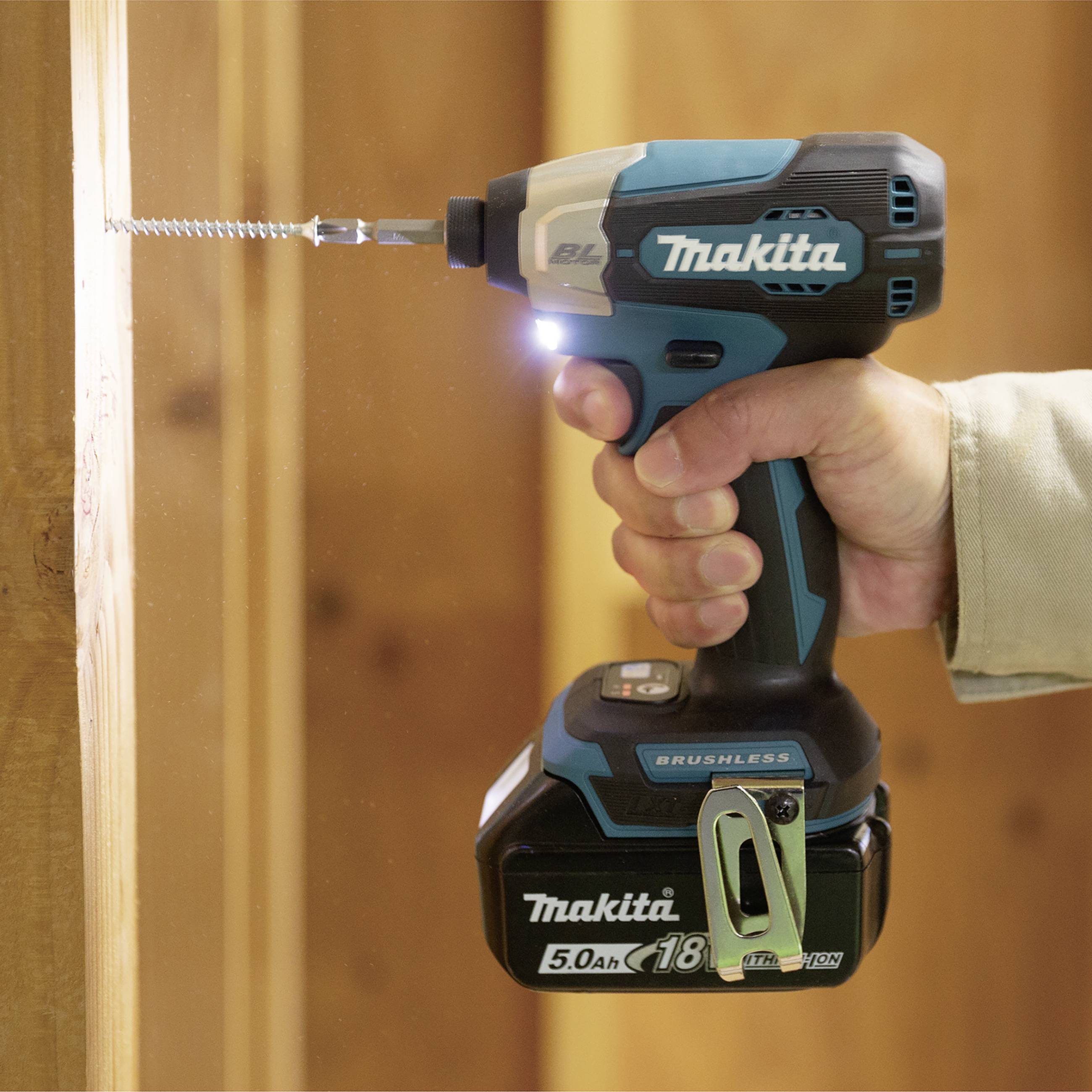Eine Person bohrt ein Loch in ein Holzbrett mit einem blauen Akku-Bohrschrauber der Marke Makita.