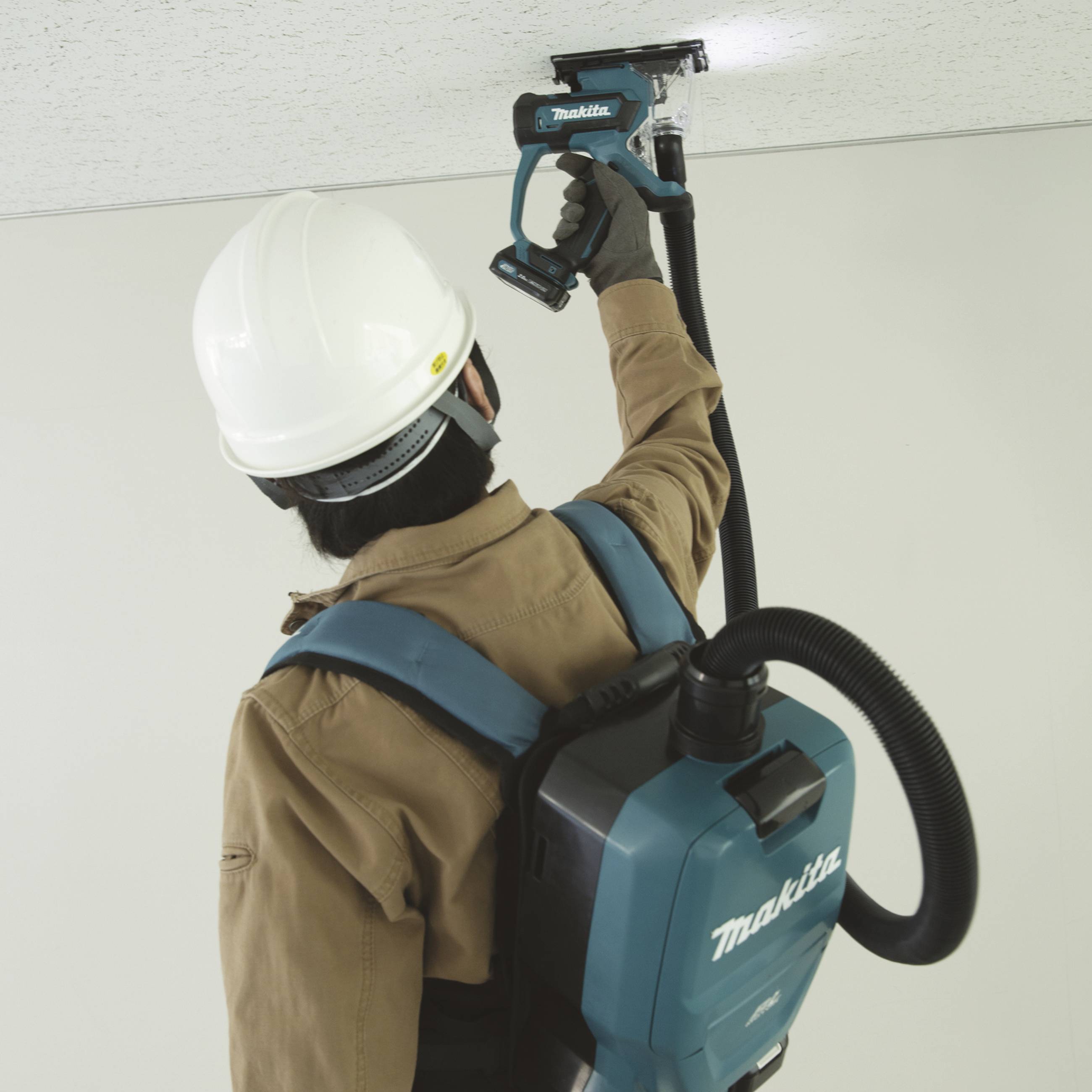 Eine Person trägt Schutzkleidung und verwendet ein tragbares Malwerkzeug an der Decke, um Farbe aufzutragen oder zu entfernen.