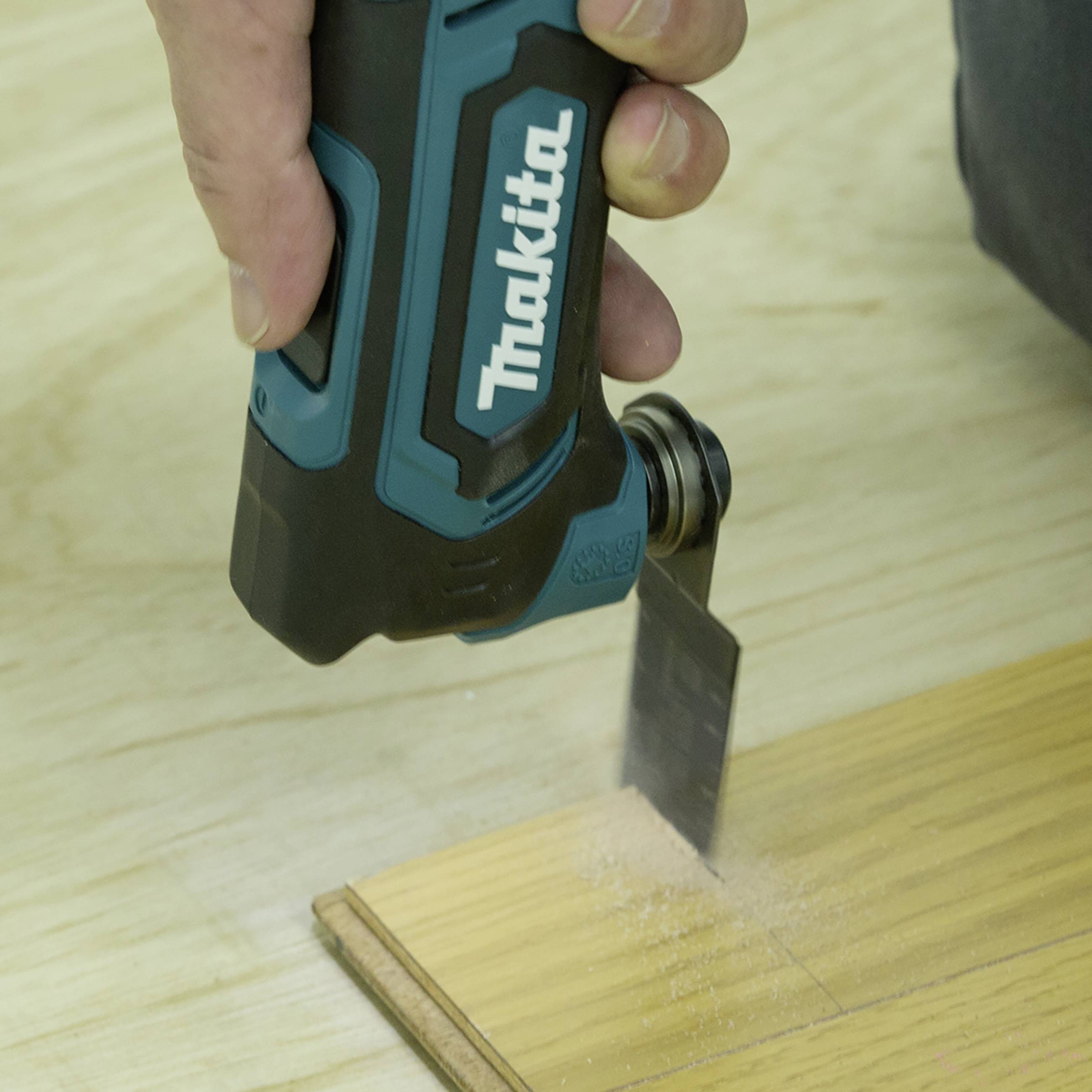 Eine Hand bedient ein Multitool-Messer, das Holz auf einem Tisch schneidet. Holzspäne sammeln sich an der Schnittstelle.
