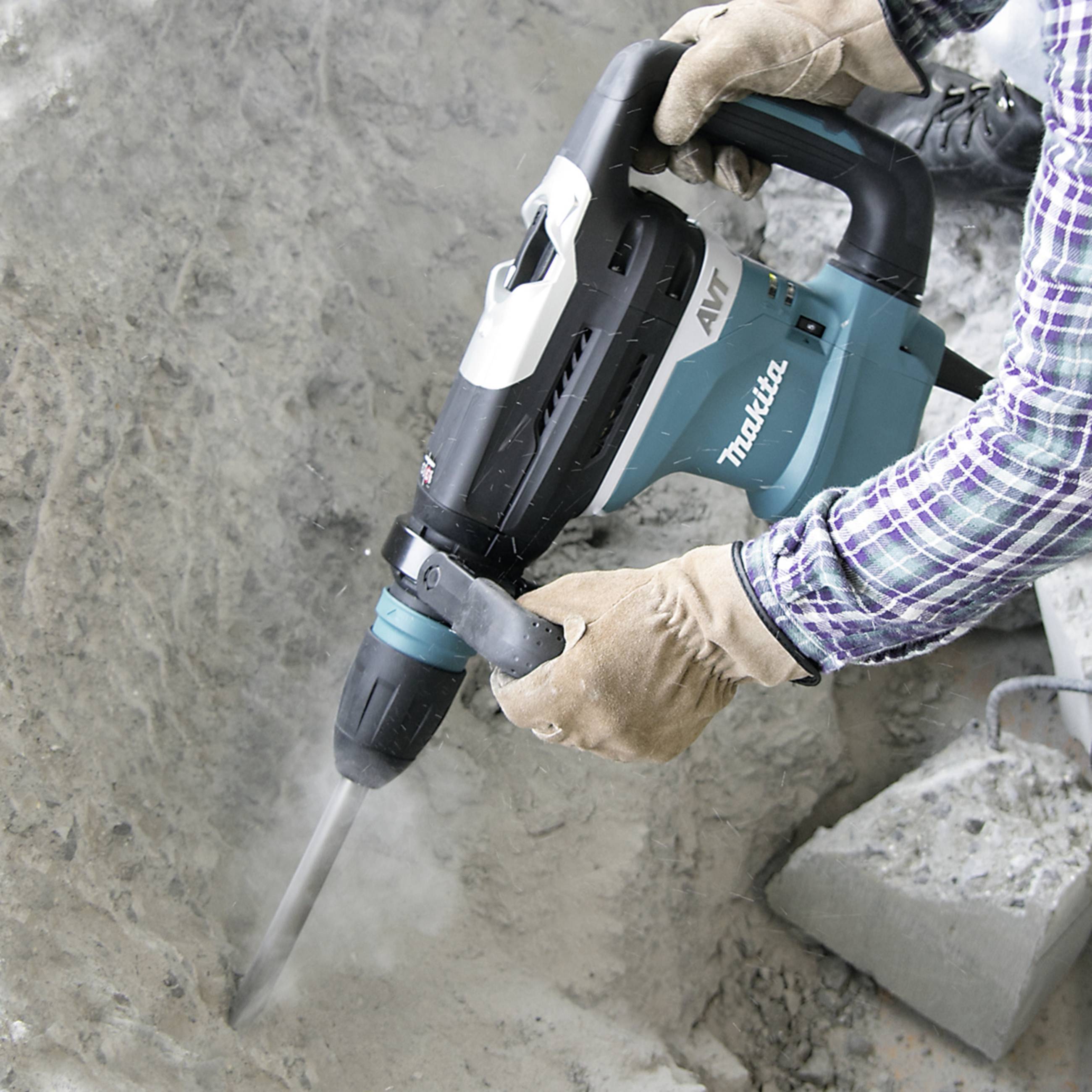 Person benutzt einen Bohrhammer, um Beton zu bearbeiten. Sicherheitskleidung wird getragen. Werkzeug ist blau-weiß-grau.