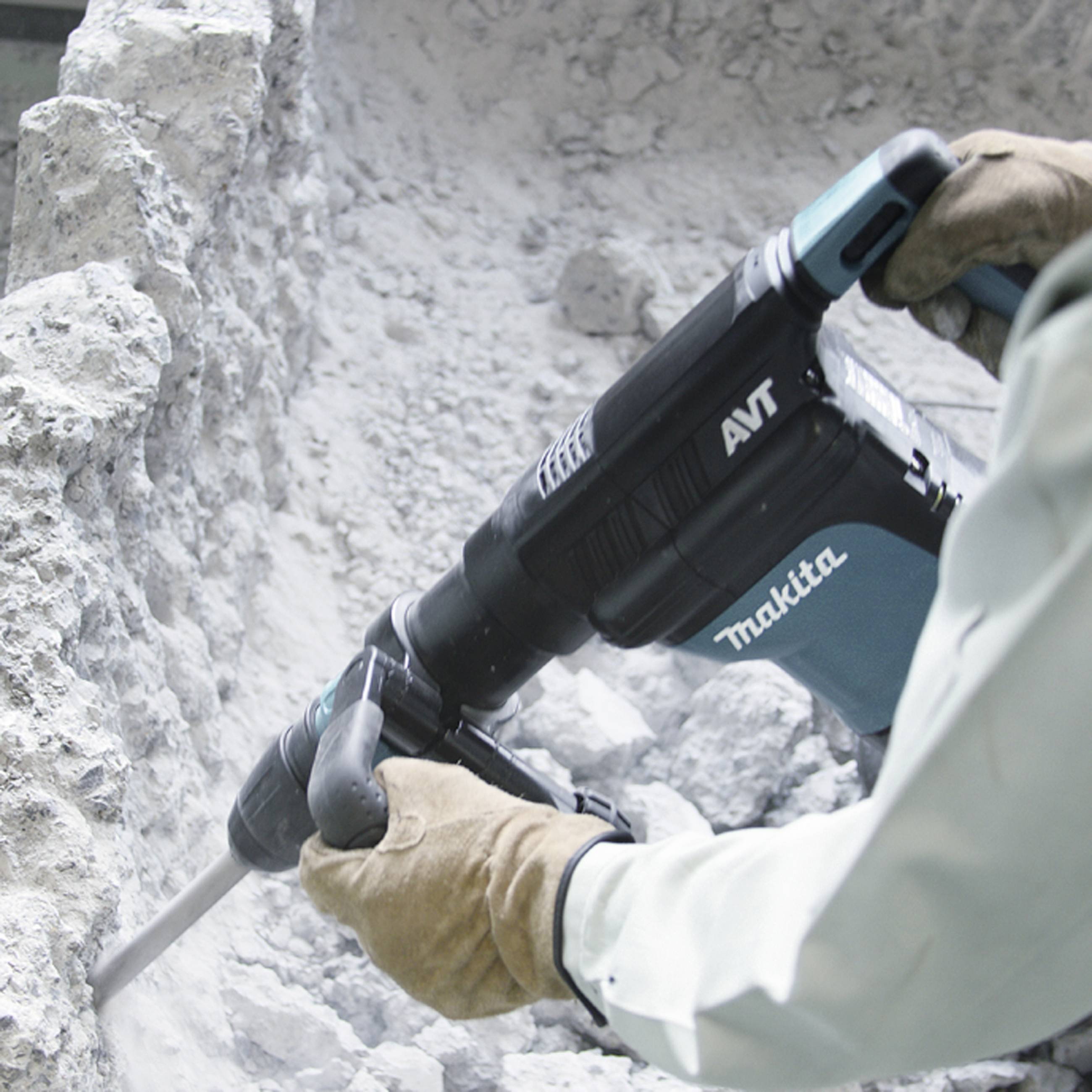 Person mit Handschuhen benutzt einen Bohrhammer zum Abtragen von Beton an einer Wand. Markierung auf dem Werkzeug: 'Makita AVT'.