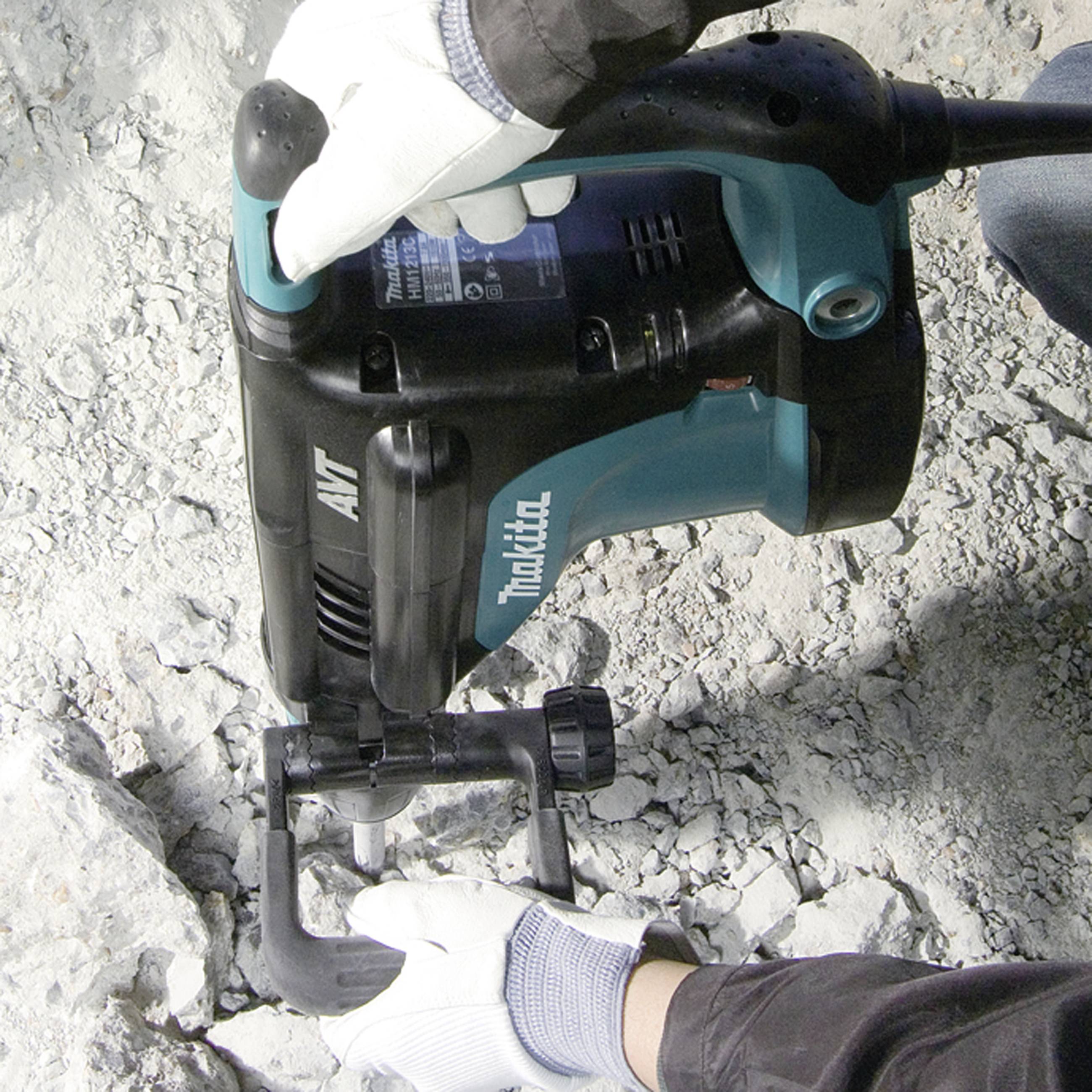 Eine Person in Arbeitskleidung benutzt einen Bohrhammer auf einer Betonfläche.