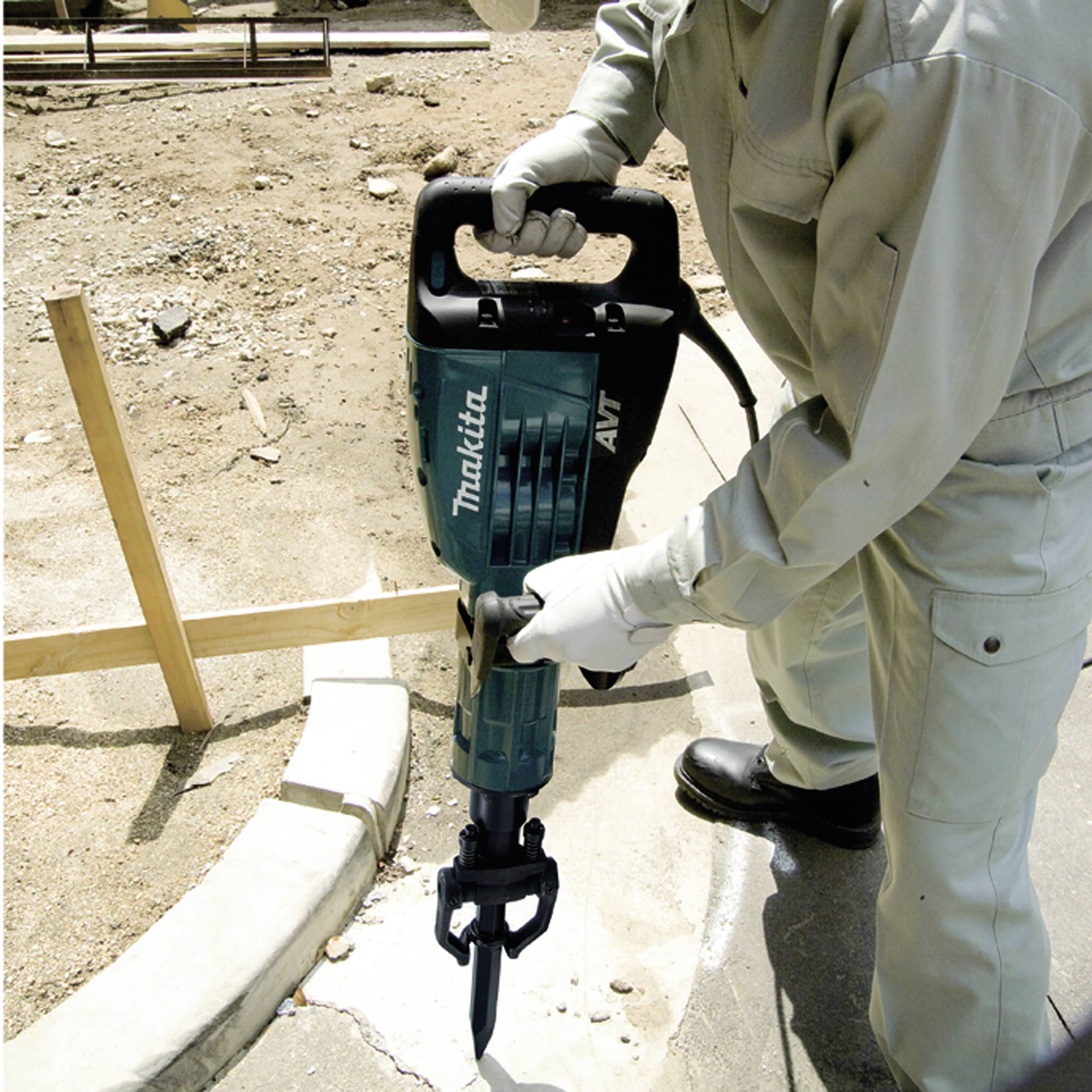 Person verwendet einen Elektrohammer auf einer Baustelle. Trägt Schutzkleidung und arbeitet an einer Betonfläche.