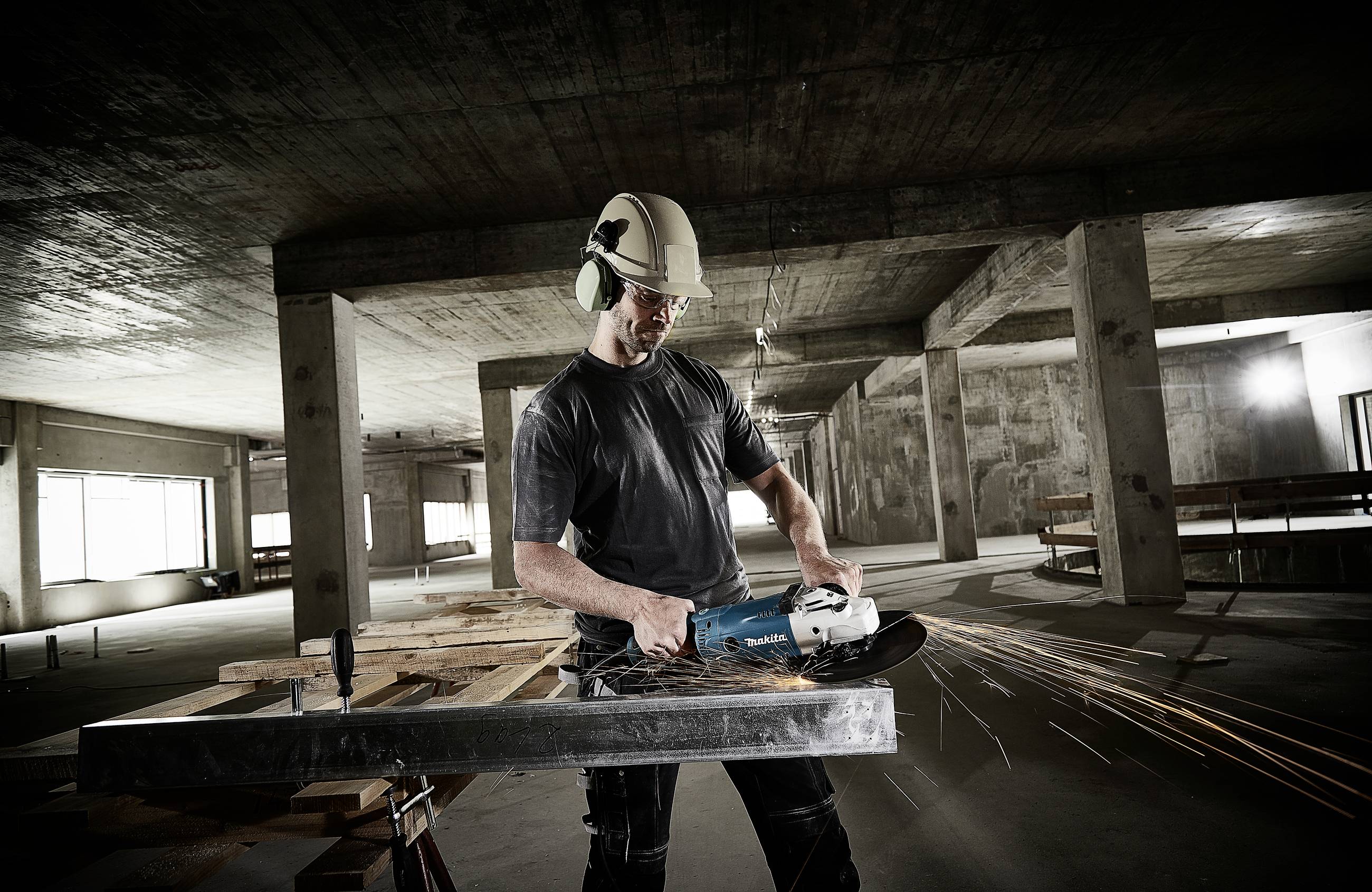 Ein Arbeiter in Schutzkleidung schneidet mit einem Winkelschleifer Metall in einem Rohbau. Funken sprühen bei der Arbeit.