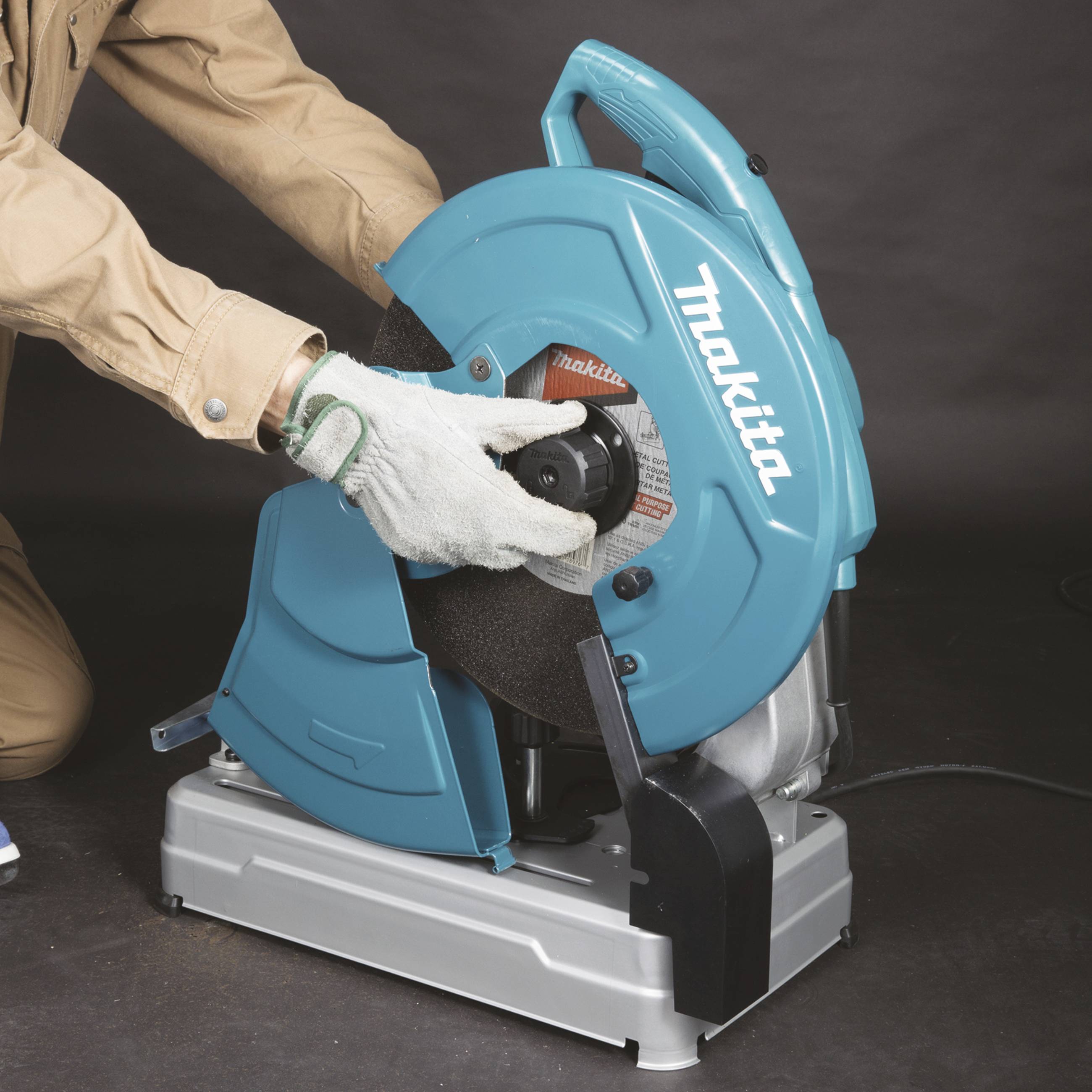 Eine Person in Arbeitskleidung benutzt eine blaue Schneidemaschine, um Metall zu schneiden. Die Person trägt Schutzhandschuhe.