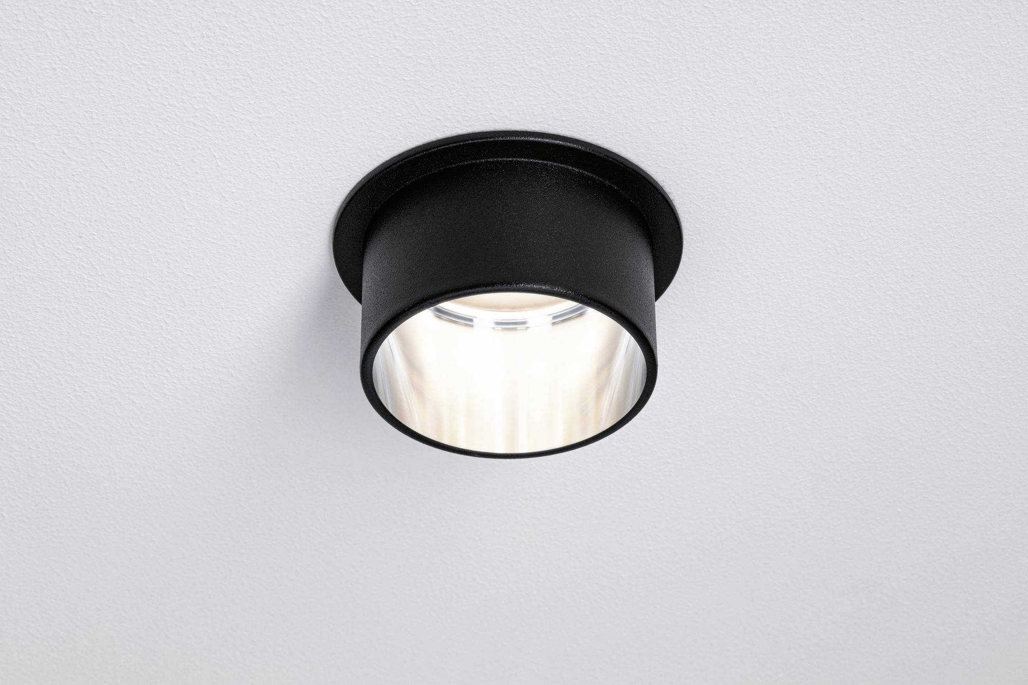 Eine schwarze Deckenleuchte aus Metall strahlt weiches, warmweißes Licht aus. Sie ist minimalistisch und modern gestaltet.