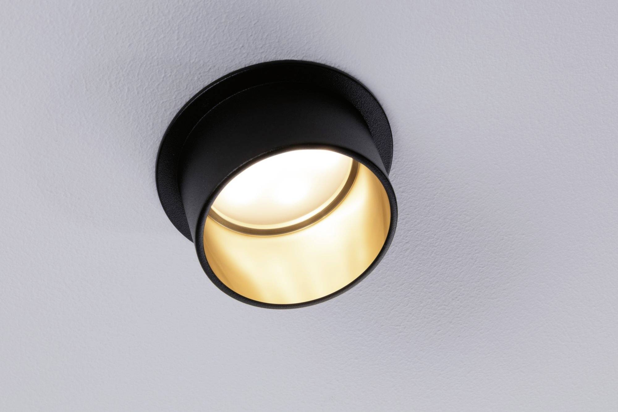 Eine Deckenlampe mit modernem, schwarzem Gehäuse und goldenem Inneren, leuchtet warmes Licht aus.
