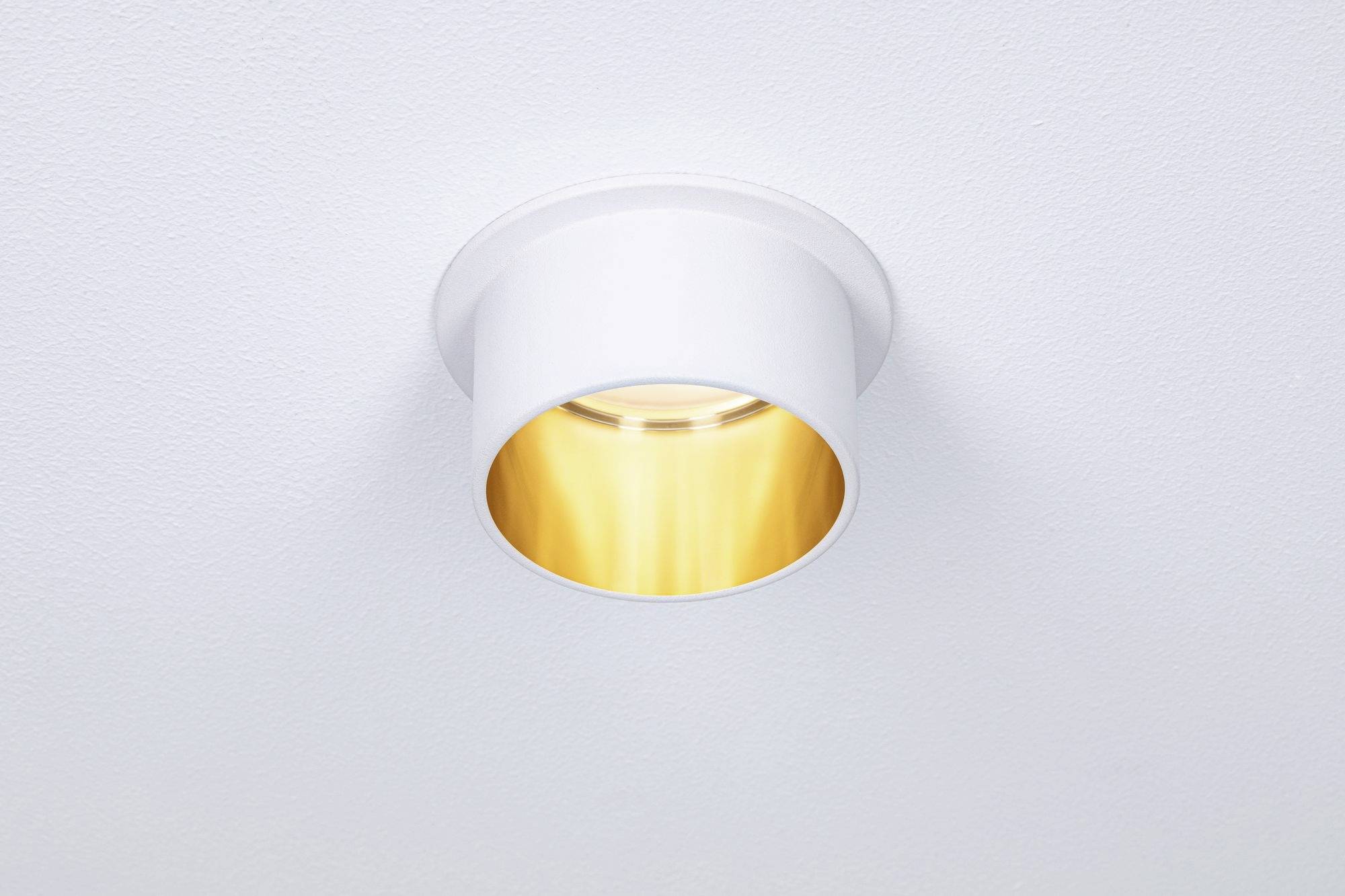 Eine runde, weiße Deckenleuchte mit goldenem Innenreflektor, die sanftes, warmes Licht auf eine weiße Decke strahlt.