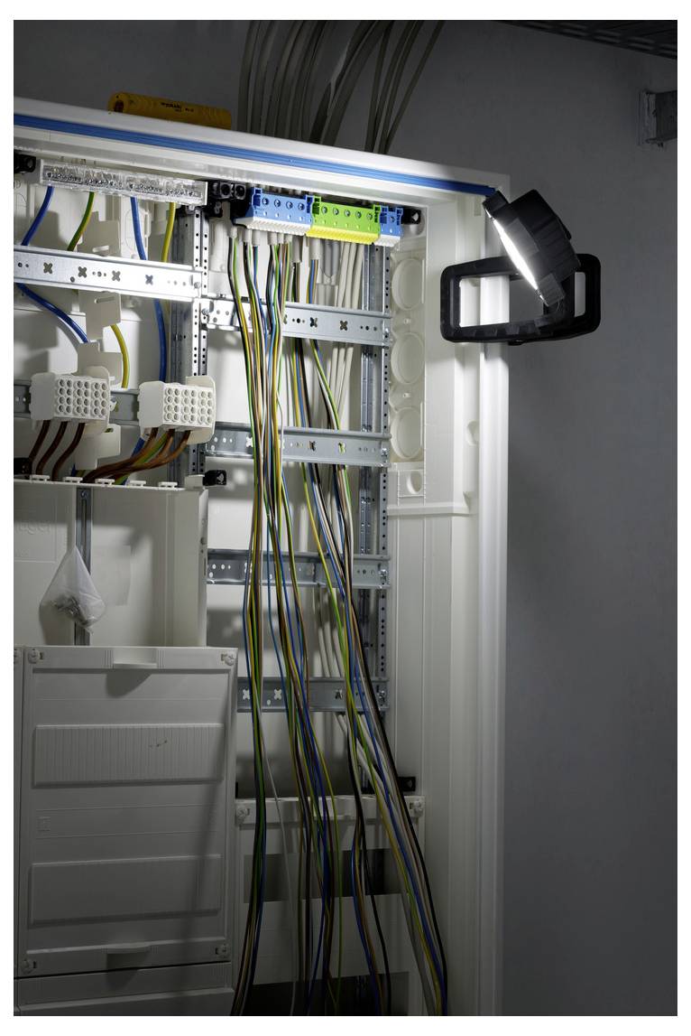 Offener Elektroschaltraum mit Reihen von Klemmenleisten und gebündelten Drähten, beleuchtet durch eine Arbeitsleuchte.