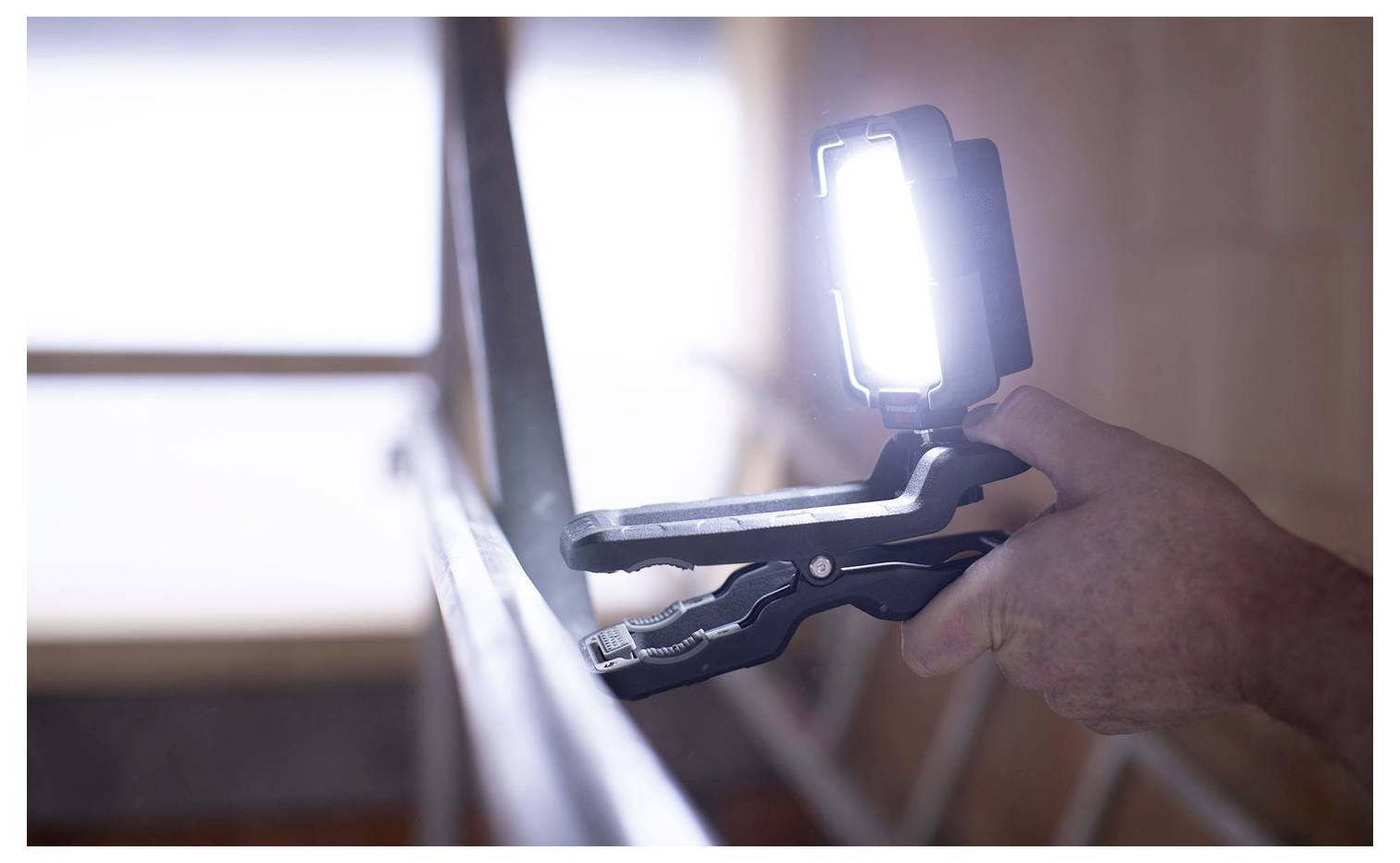 Person, die eine tragbare LED-Arbeitsleuchte verwendet, die an einer Halterung angebracht ist, während sie drinnen arbeitet, mit hellem Licht, das auf die Oberfläche gerichtet ist.
