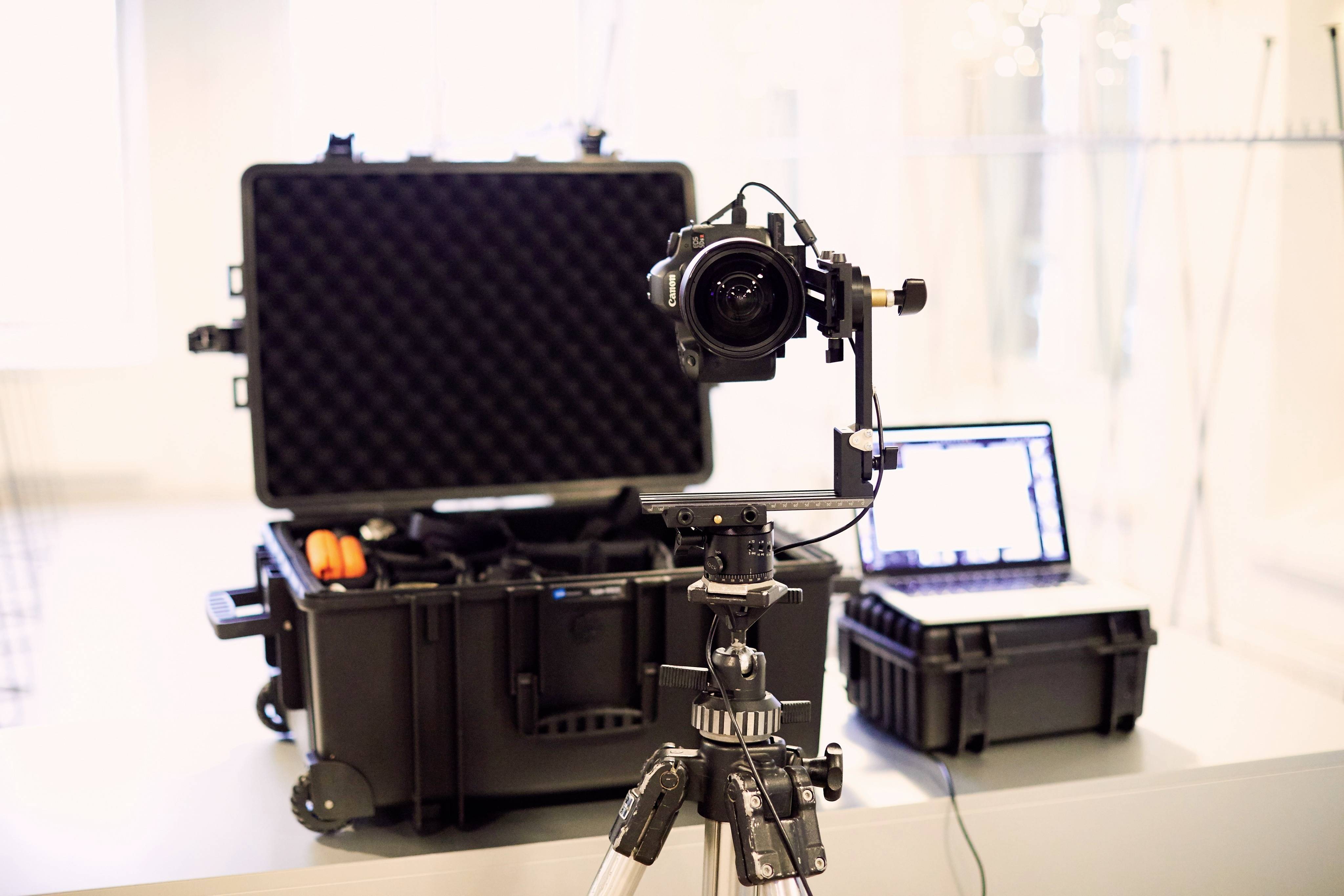 Eine Kamera auf einem Stativ vor einem offenen Koffer und einem Laptop; Bereitstellung für eine Foto- oder Videoaufnahme.