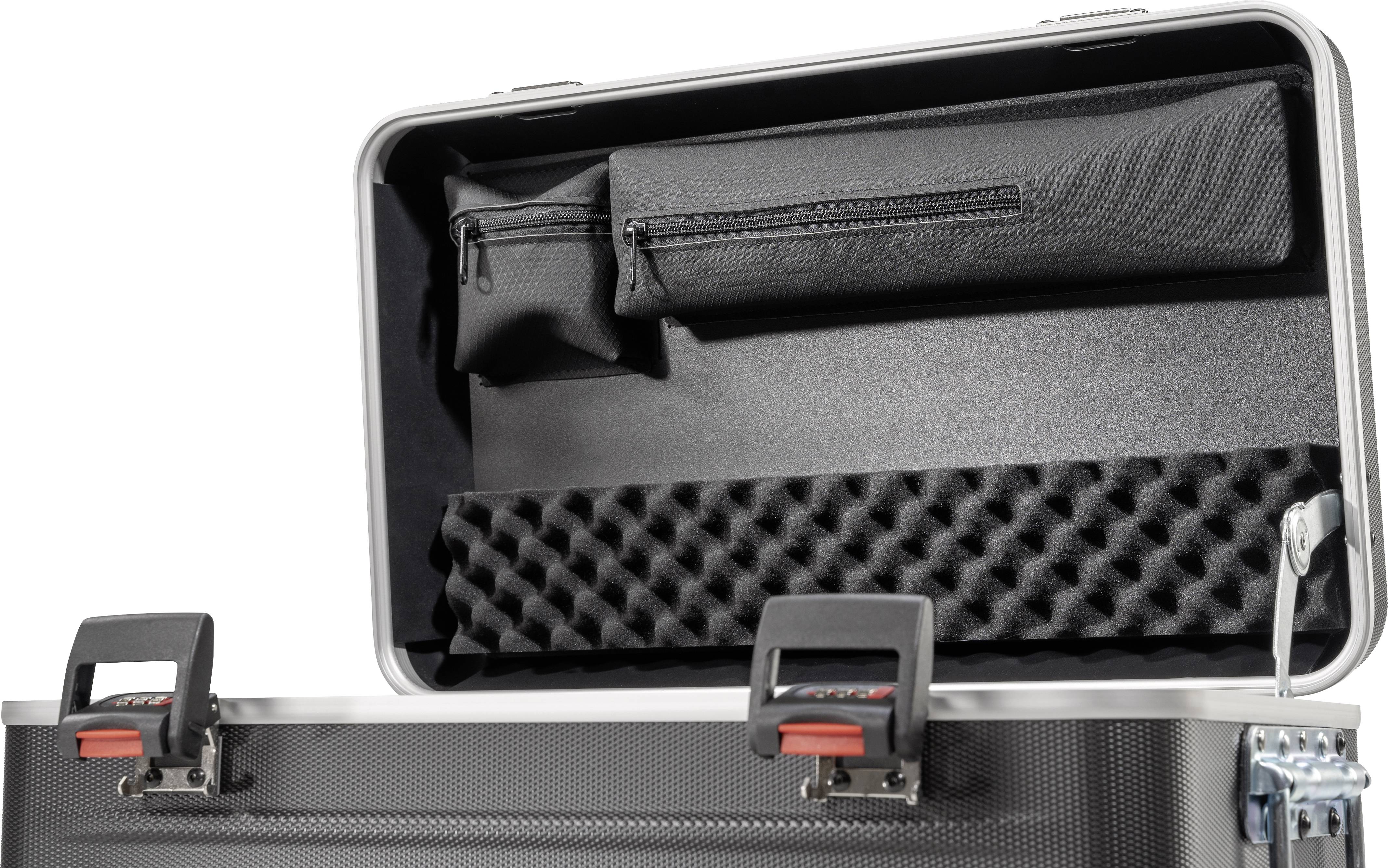 Offener schwarzer Koffer mit Schaumstoffpolsterung und zwei Reißverschlusstaschen im Deckel. Kofferschlösser stehen offen.