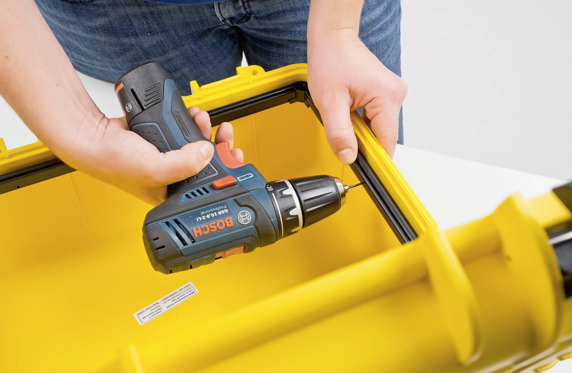 Person montiert mit einem blauen Akkuschrauber von Bosch ein gelbes, rechteckiges Objekt. Focus liegt auf der Schraubaktion.