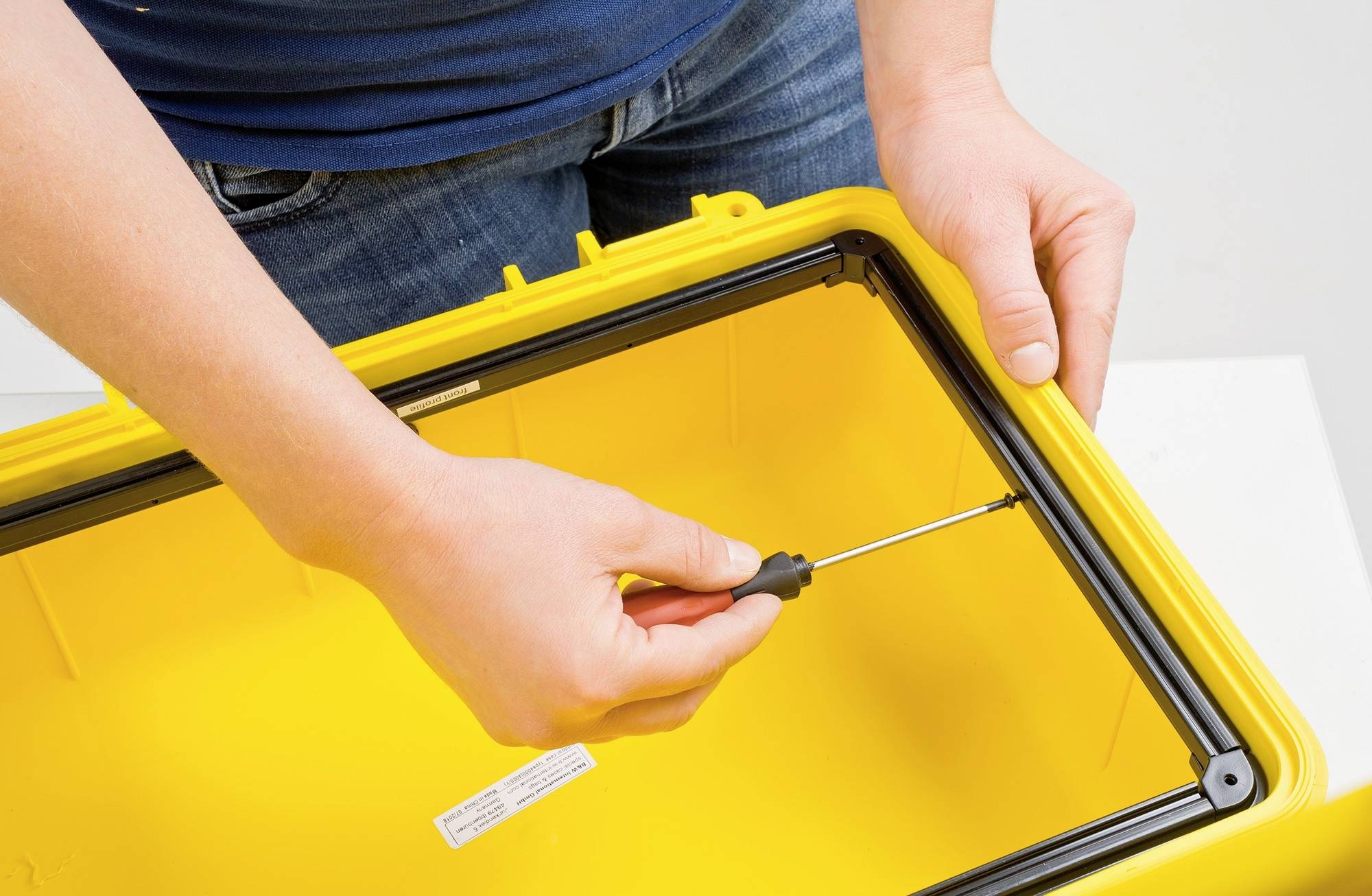 Eine Person schraubt an einem gelben Kunststoffkasten. Sie verwendet einen Schraubendreher, um den Deckel zu sichern.